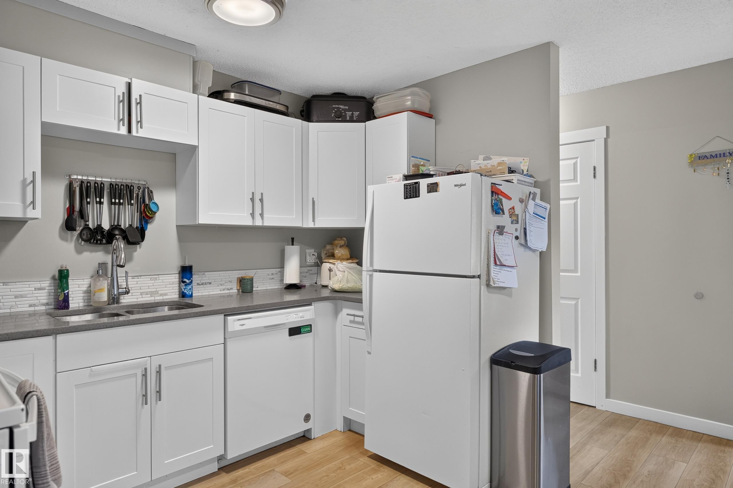 Kitchen featuring white cabinetry, a double basin sink, white appliances, light wood-finish flooring, and a patterned backsplash - 18319 93 Avenue Nw, Edmonton, AB