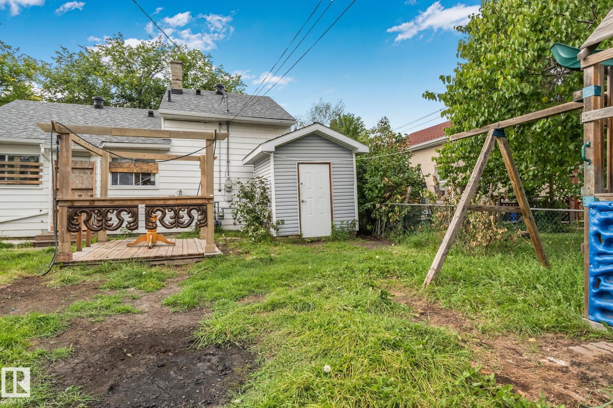 Backyard featuring a wooden deck with decorative railing, an exterior shed with horizontal siding, and mature perimeter trees - 11935 125 Street Nw, Edmonton, AB