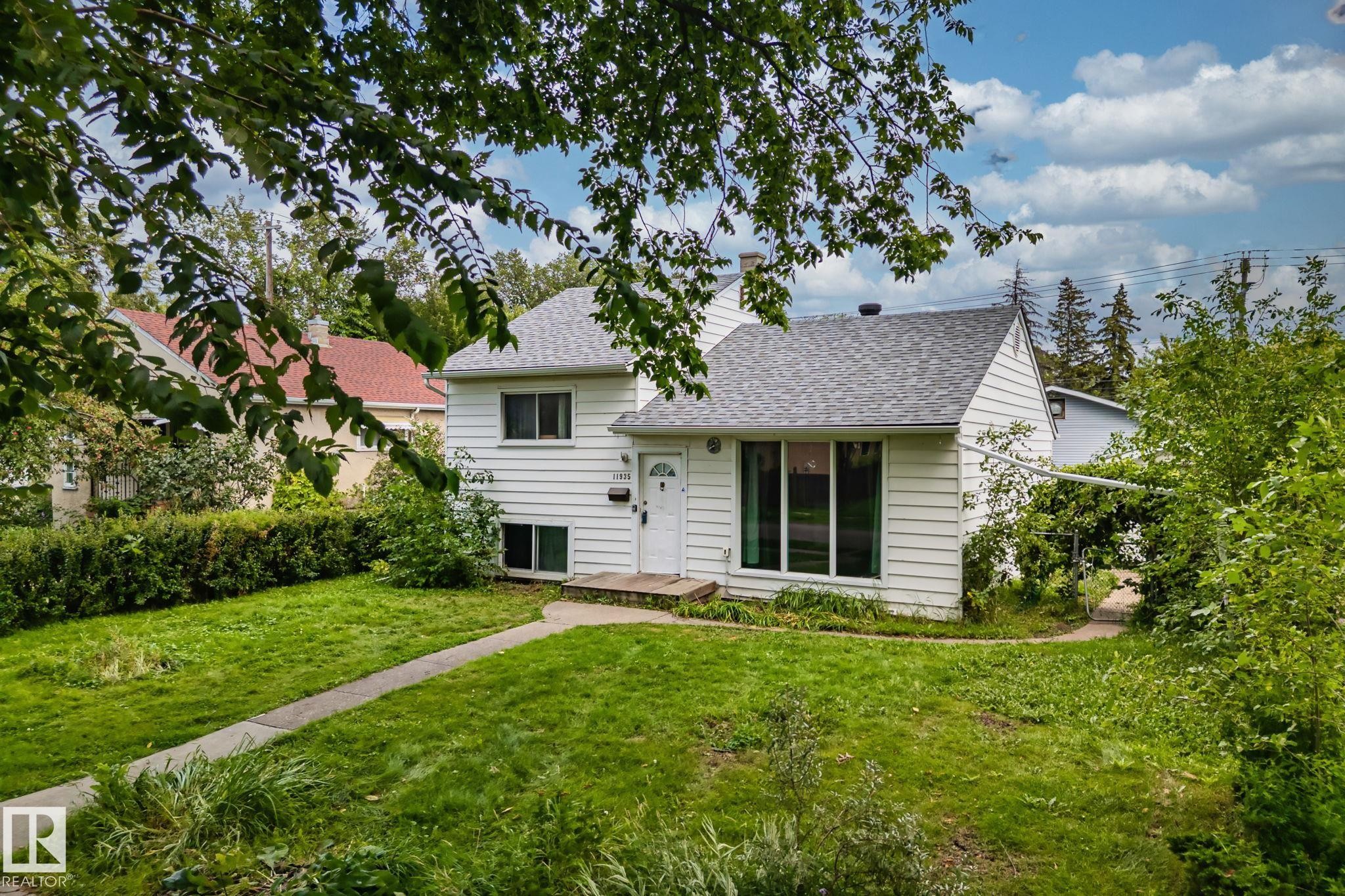 White-sided exterior with a light gray shingled roof, a paved walkway, and a front yard with mature greenery - 11935 125 Street Nw, Edmonton, AB