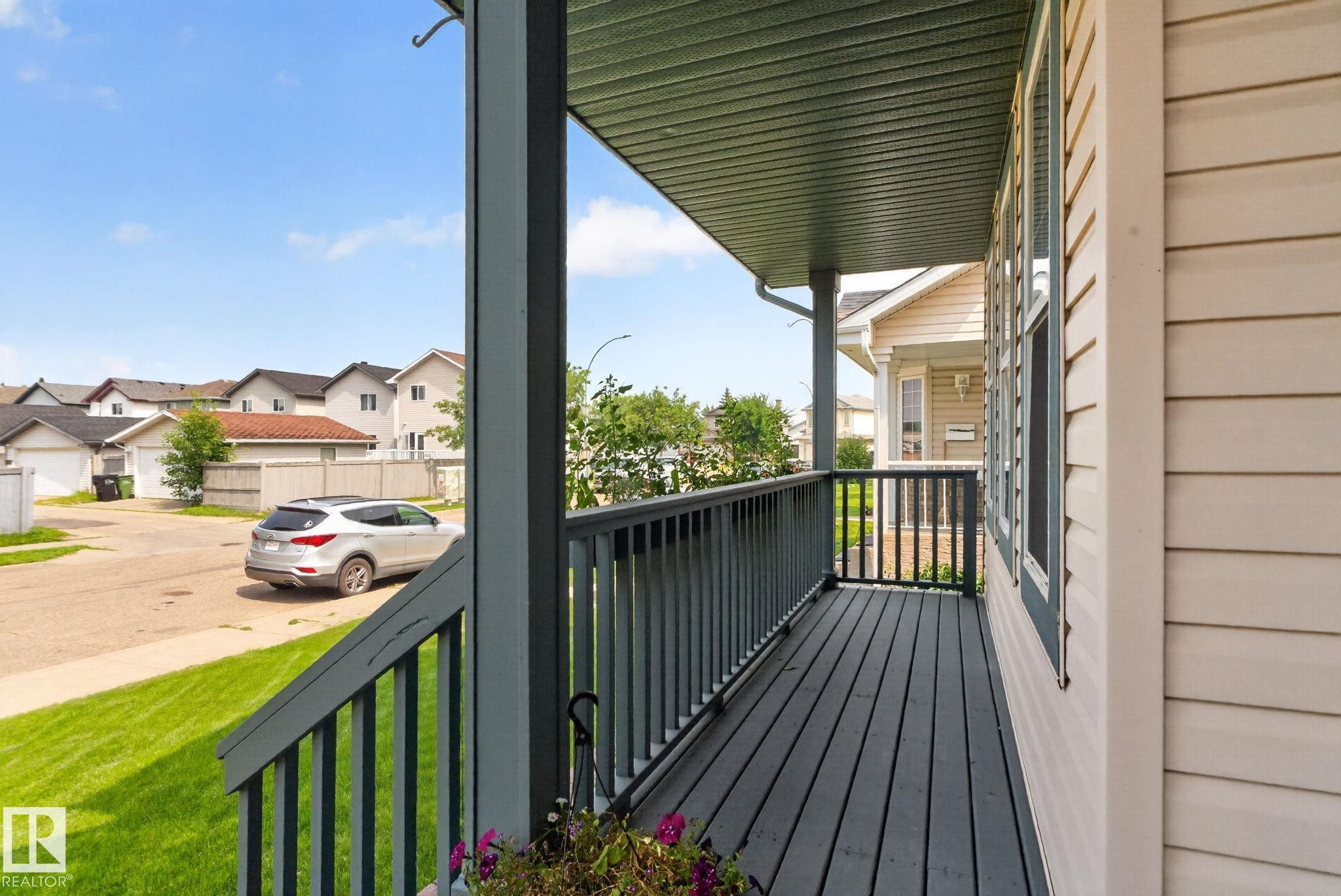 Covered porch featuring dark wood-finish decking and railing with a contrasting light-colored siding - 8923 173 Avenue Nw, Edmonton, AB