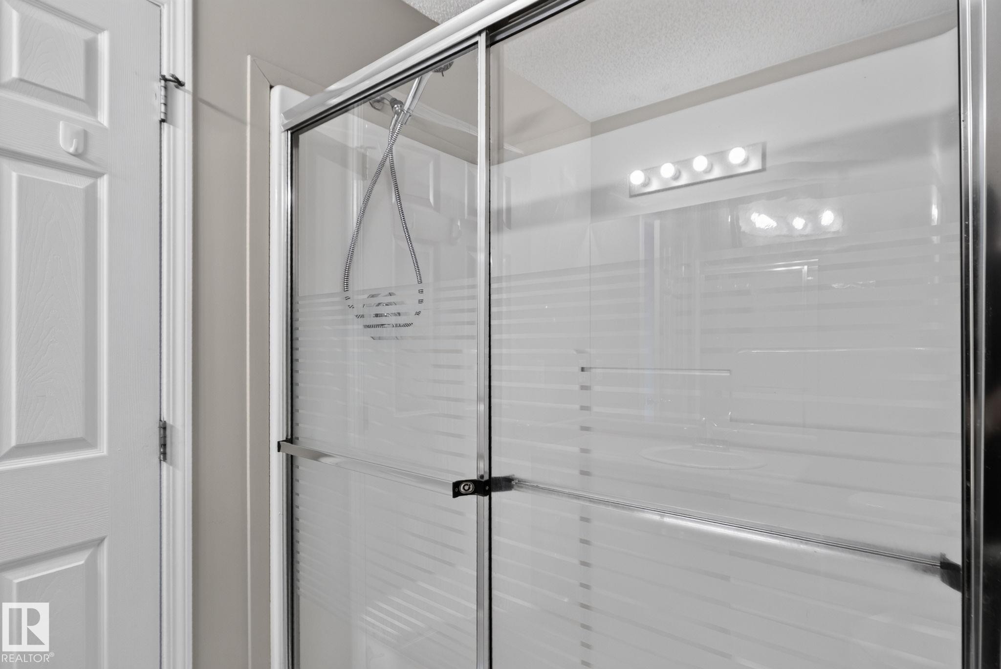 Enclosed shower with clear glass door, chrome hardware, and integrated lighting fixture - 8923 173 Avenue Nw, Edmonton, AB
