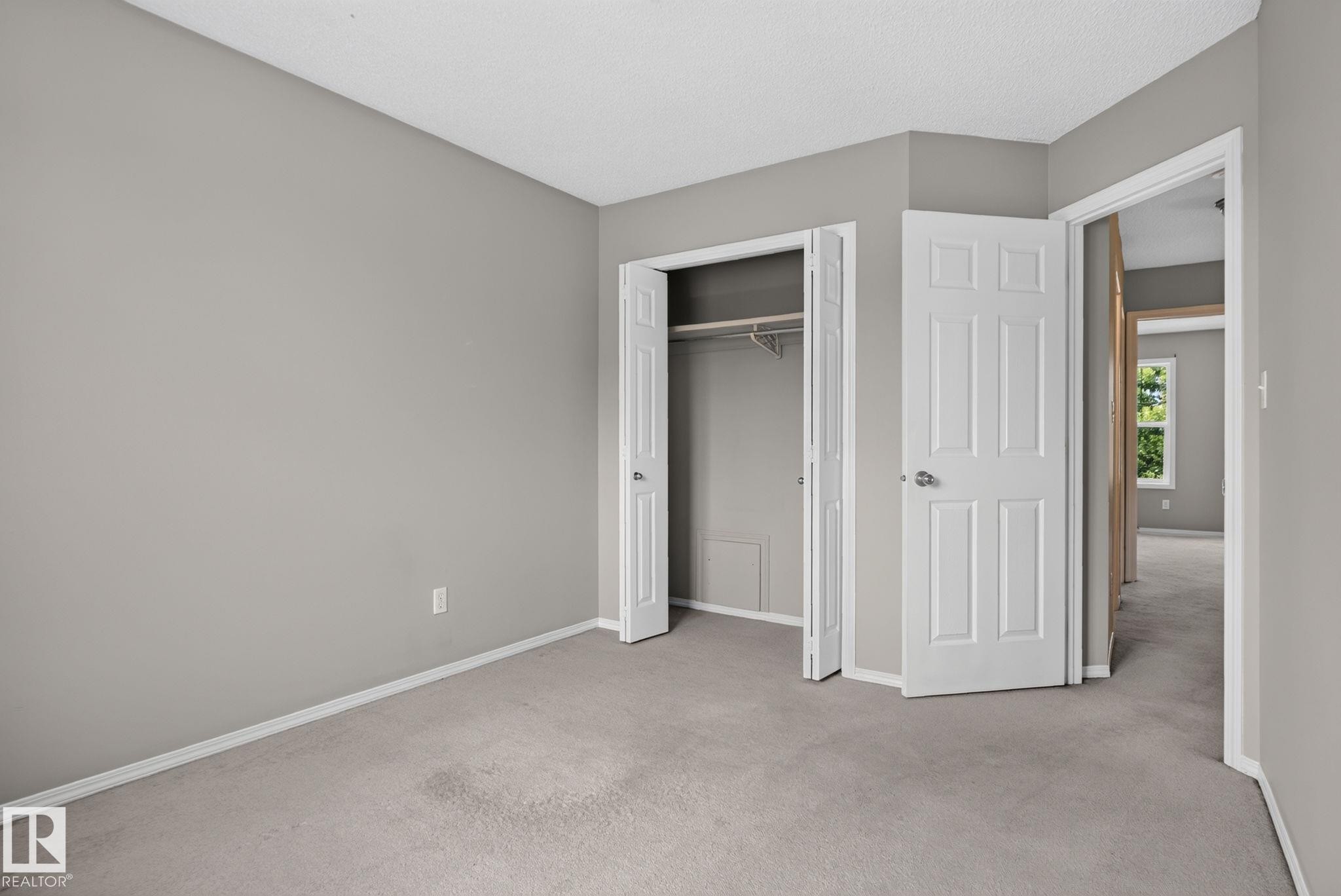 Neutral gray wall paint, light gray carpet flooring, white trim, bifold closet doors, and a paneled interior door - 8923 173 Avenue Nw, Edmonton, AB
