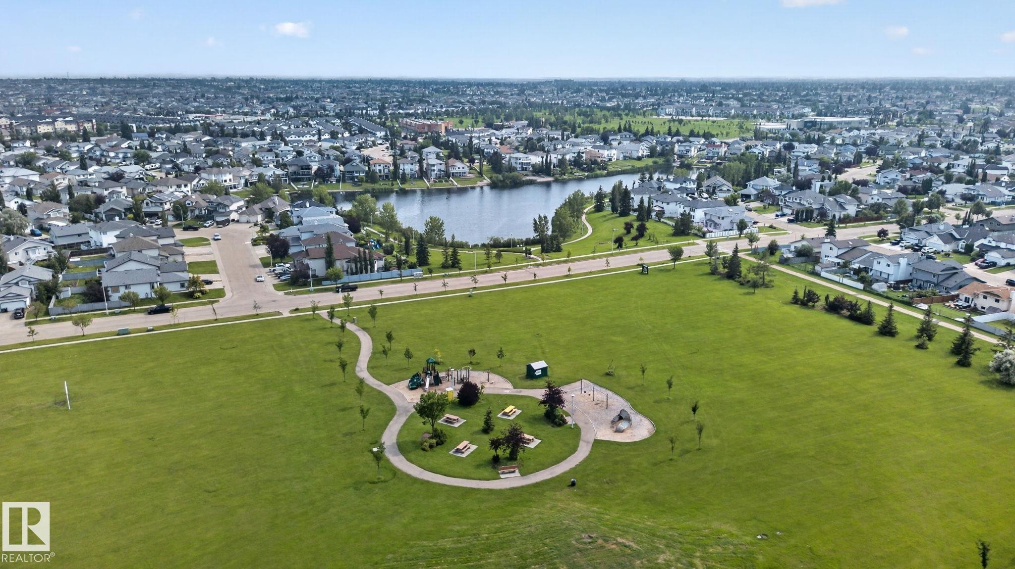 Expansive green space featuring a playground, paved walking paths, and a nearby lake - 8923 173 Avenue Nw, Edmonton, AB