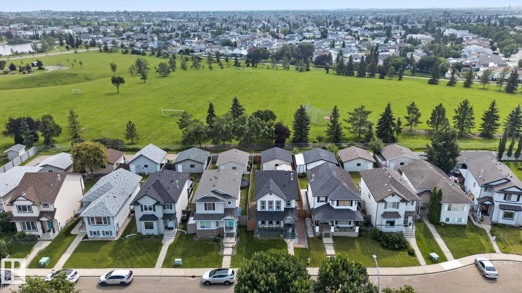 Aerial perspective of a residential street featuring detached homes with front yards, bordered by a large green space - 8923 173 Avenue Nw, Edmonton, AB
