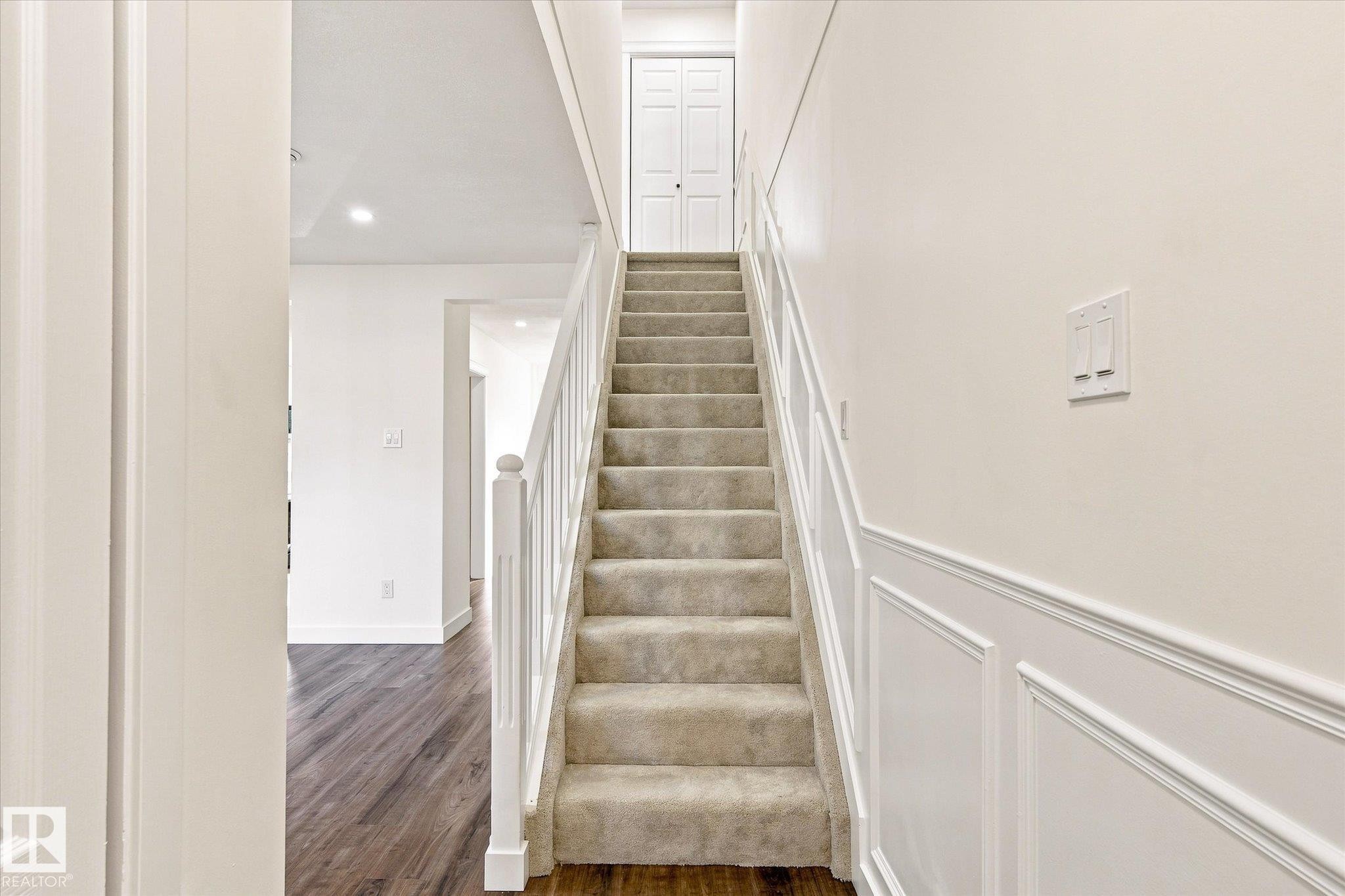 Carpeted staircase with white balusters, wainscoting detail, and recessed lighting - 17325 85 Avenue Nw, Edmonton, AB
