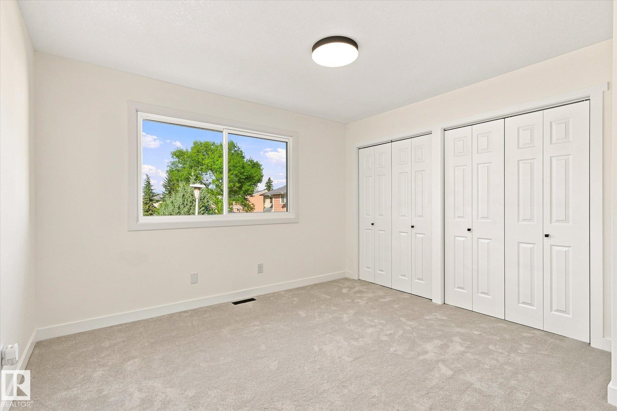 Light neutral wall color, light gray carpet, multiple bi-fold closet doors, contemporary flush-mount ceiling light, and a large window with white trim - 17325 85 Avenue Nw, Edmonton, AB