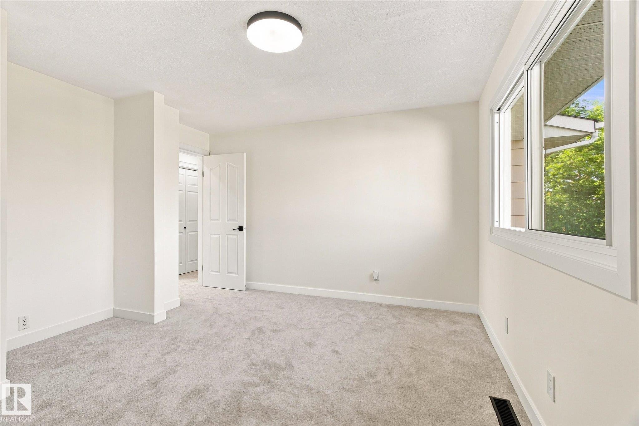 Light gray wall-to-wall carpeting, white interior walls, white window trim, white interior door, and a flush mount ceiling light fixture - 17325 85 Avenue Nw, Edmonton, AB