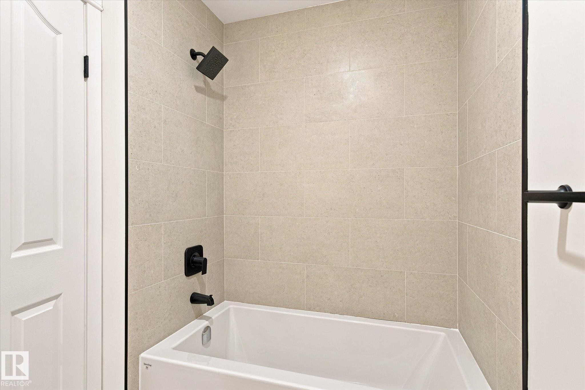 Bathtub with matte black fixtures, light-toned wall tiling, and a white paneled door - 17325 85 Avenue Nw, Edmonton, AB
