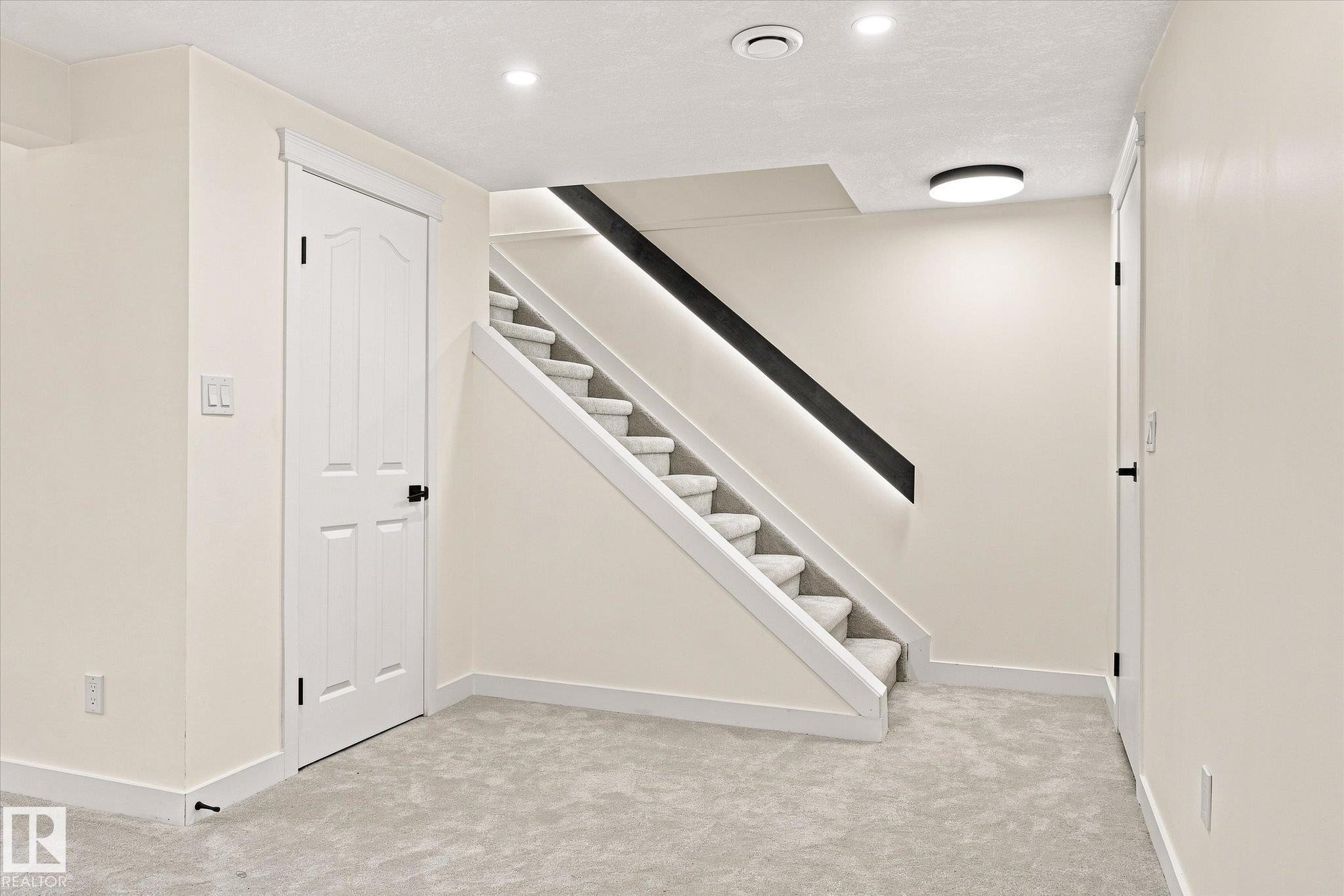 Staircase featuring carpeted treads and a modern black handrail with integrated lighting - 17325 85 Avenue Nw, Edmonton, AB