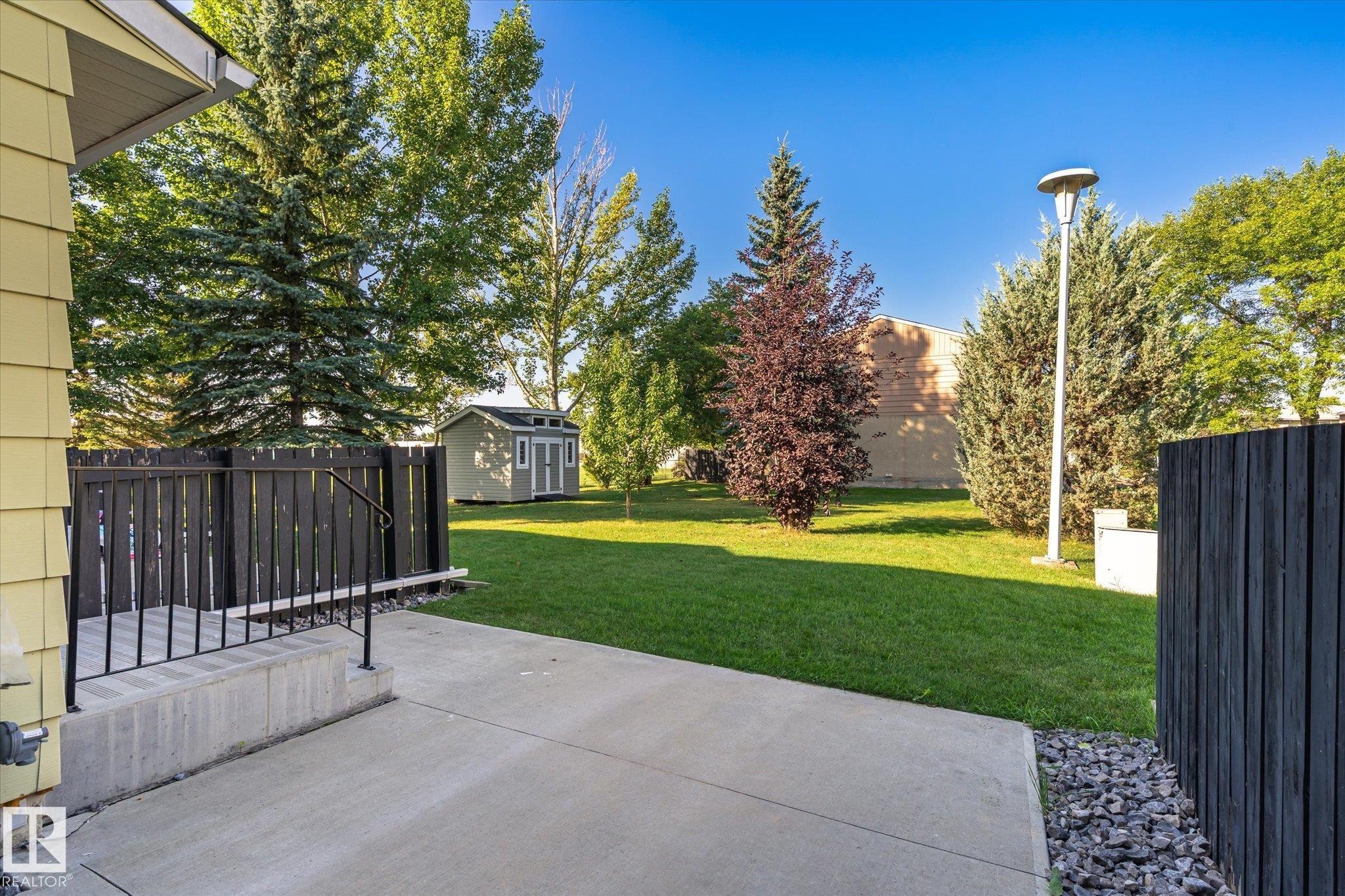 Expansive lawn area with mature trees, concrete patio, and a dedicated storage shed - 17325 85 Avenue Nw, Edmonton, AB