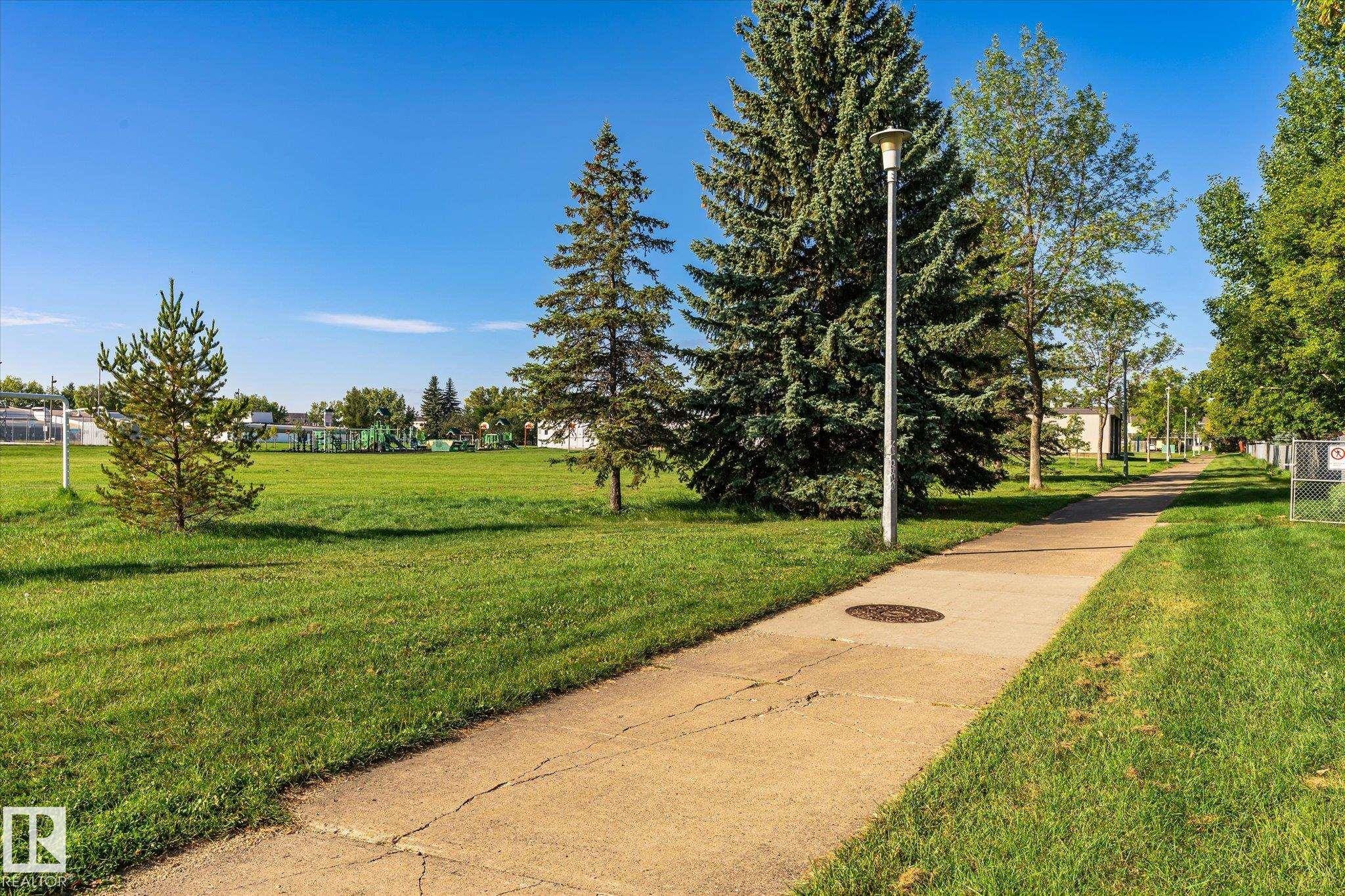 Paved pathway bordered by manicured lawns and mature evergreen trees - 17325 85 Avenue Nw, Edmonton, AB