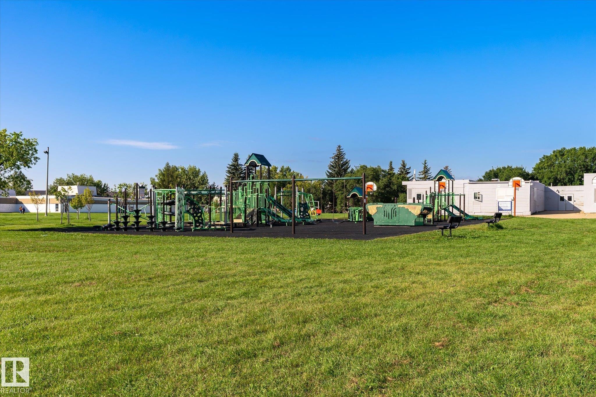 Expansive green space featuring a multi-component playground structure, integrated slides, swing sets, and basketball hoops, all set on a dark-toned safety surface - 17325 85 Avenue Nw, Edmonton, AB