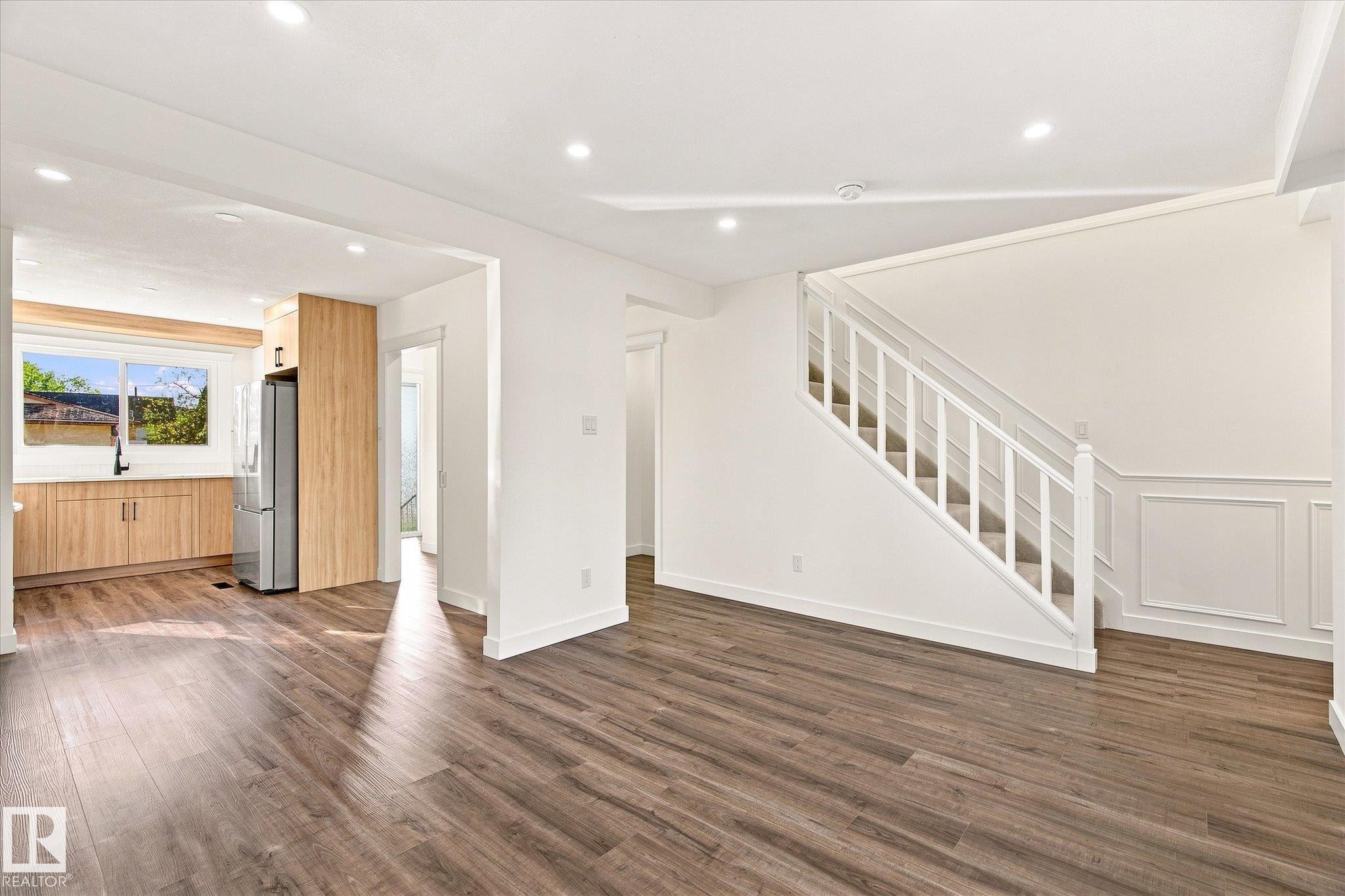 Expansive living area with wood-finish flooring, recessed lighting, and a modern staircase with white balusters - 17325 85 Avenue Nw, Edmonton, AB