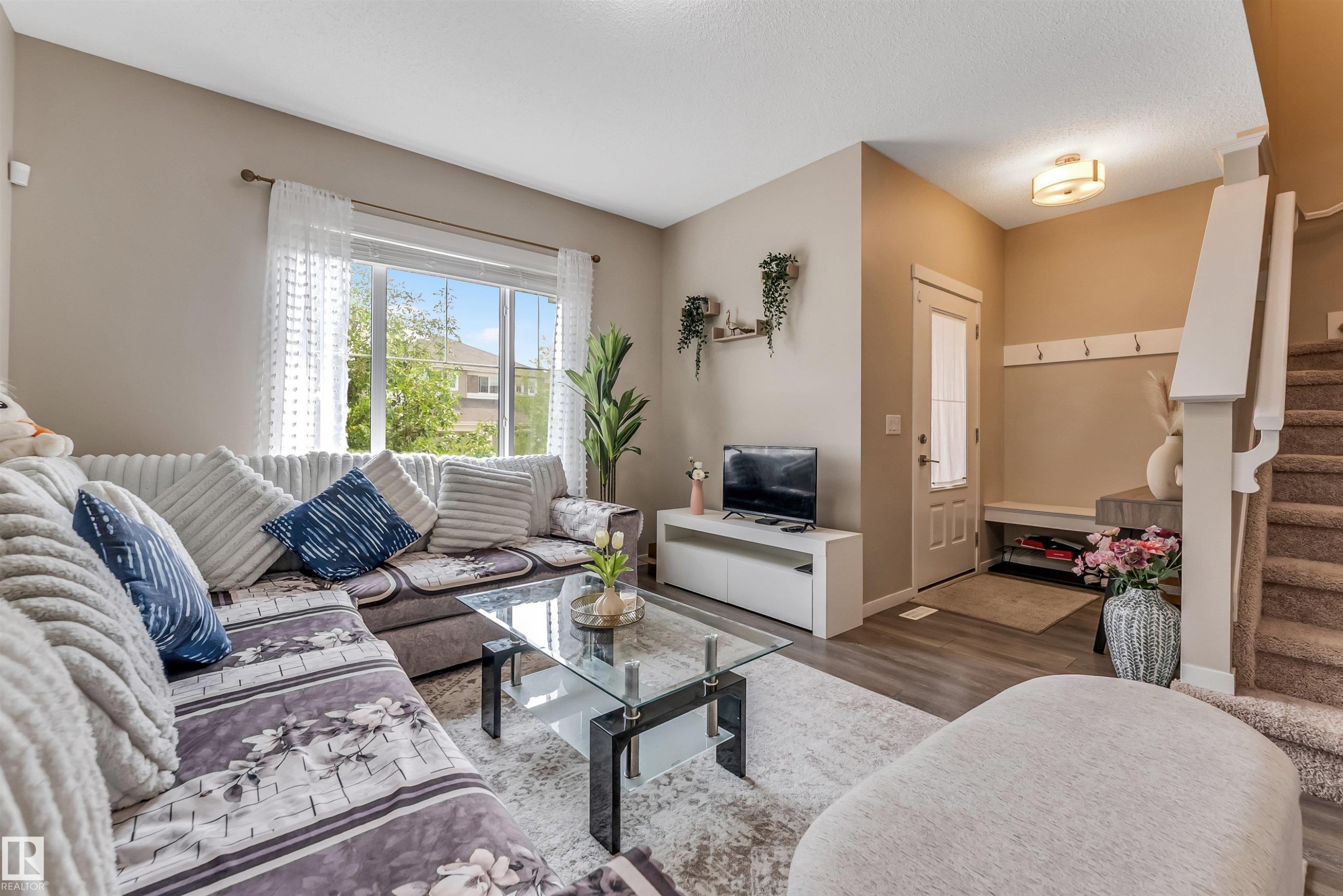 Bright living area featuring large windows, wood-finish flooring, a built-in entry bench, and carpeted stairs - 1514 26 Avenue Nw, Edmonton, AB - Indoor Photo Showing Living Room