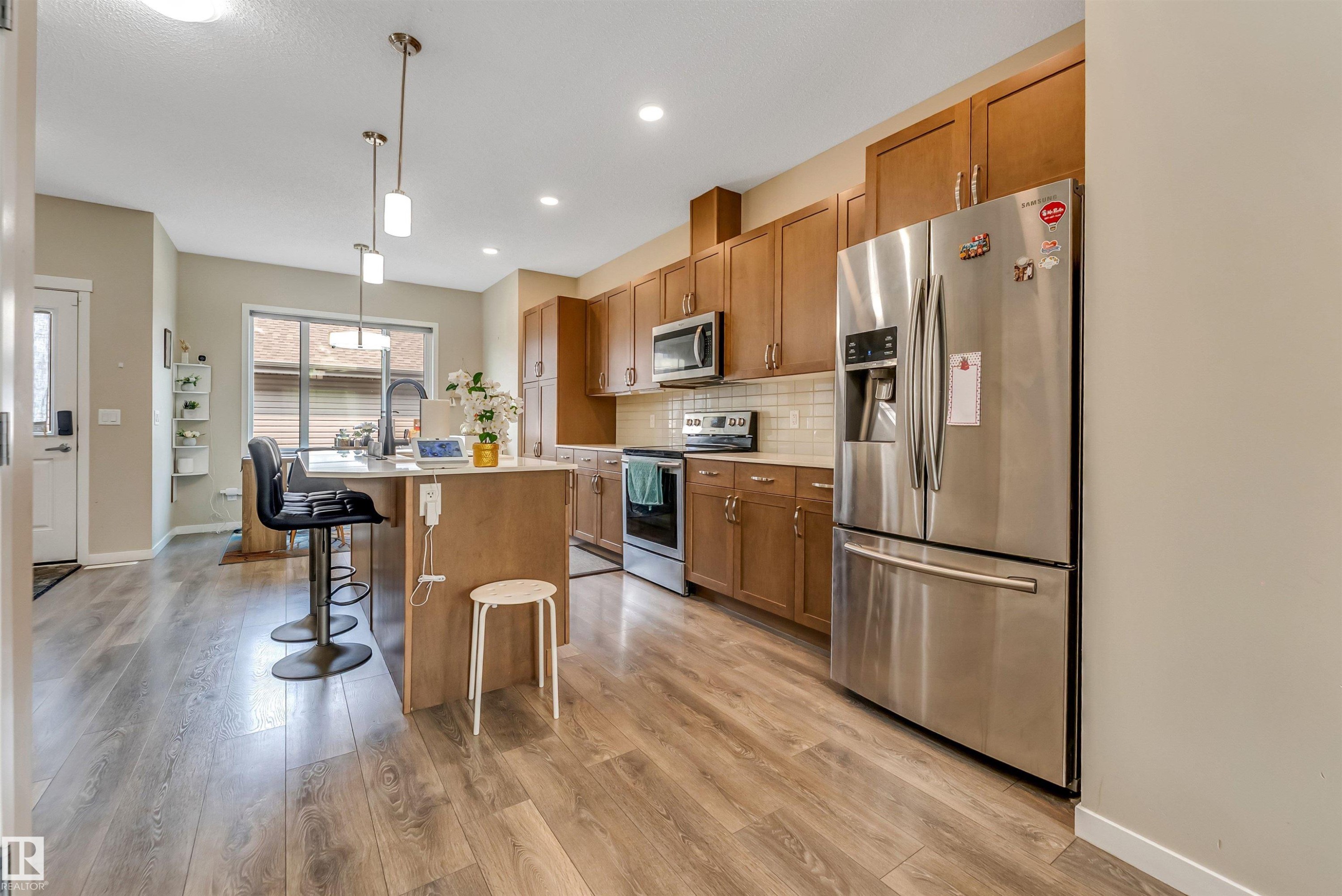 Open-concept kitchen featuring wood-finish flooring, stainless steel appliances, a center island with pendant lighting, wood cabinetry, and a subway tile backsplash - 1514 26 Avenue Nw, Edmonton, AB - Indoor Photo Showing Kitchen With Upgraded Kitchen