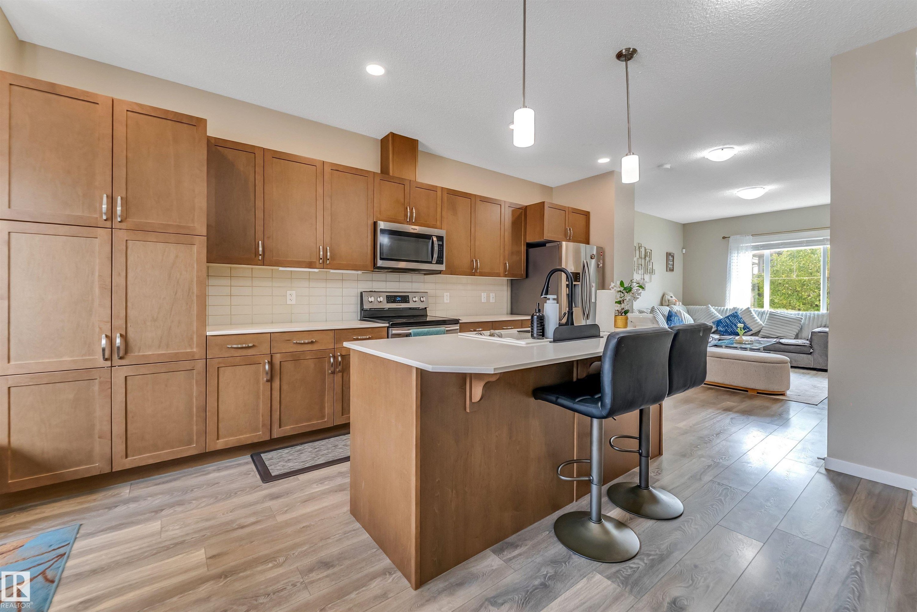 Contemporary kitchen featuring wood-finish cabinetry, stainless steel appliances, a subway tile backsplash, and a central island with pendant lighting - 1514 26 Avenue Nw, Edmonton, AB - Indoor Photo Showing Kitchen With Upgraded Kitchen