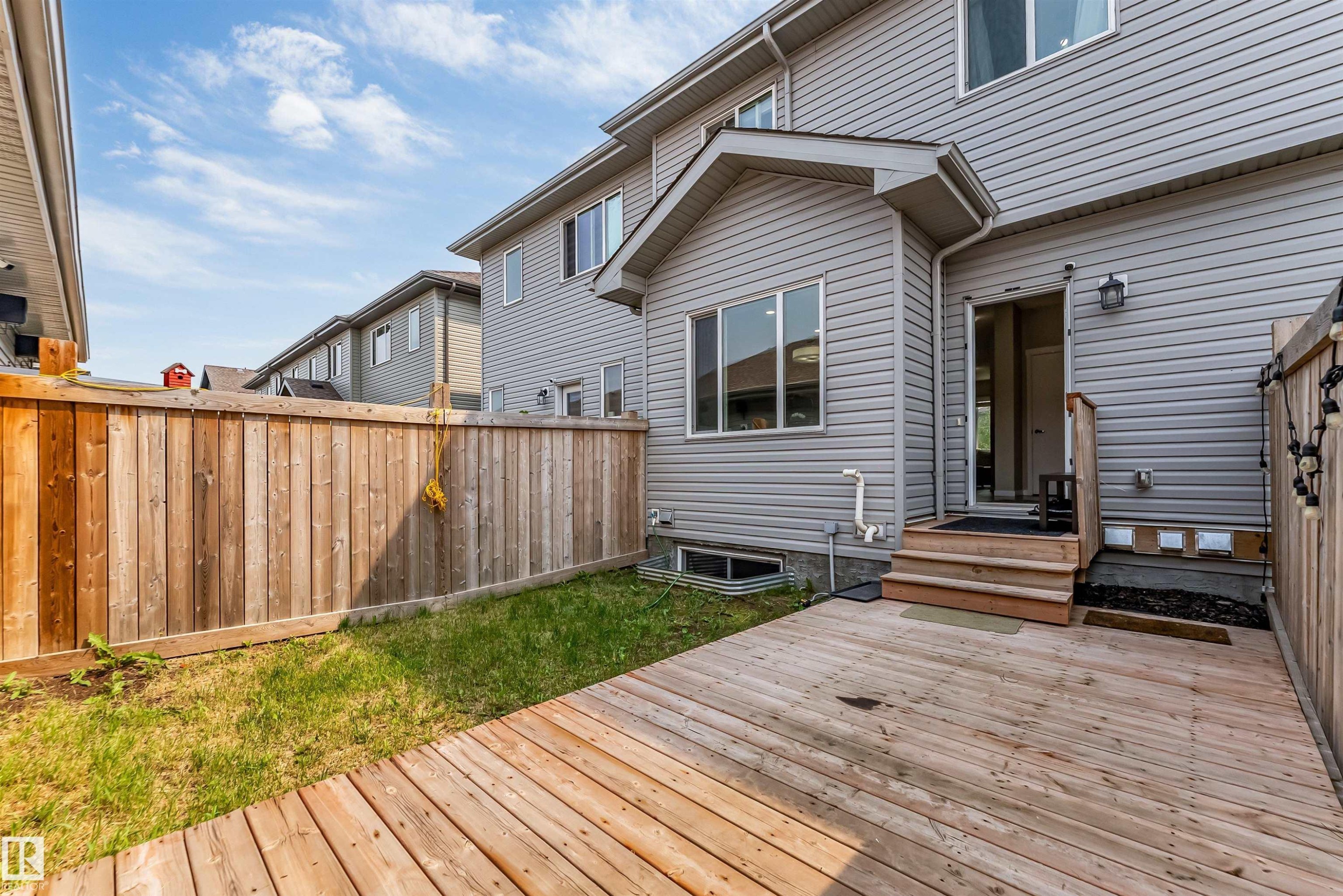 Rear exterior featuring a wooden deck with stairs to an entryway, gray siding, a window with white trim, a privacy fence, and a patch of grass - 1514 26 Avenue Nw, Edmonton, AB - Outdoor With Deck Patio Veranda