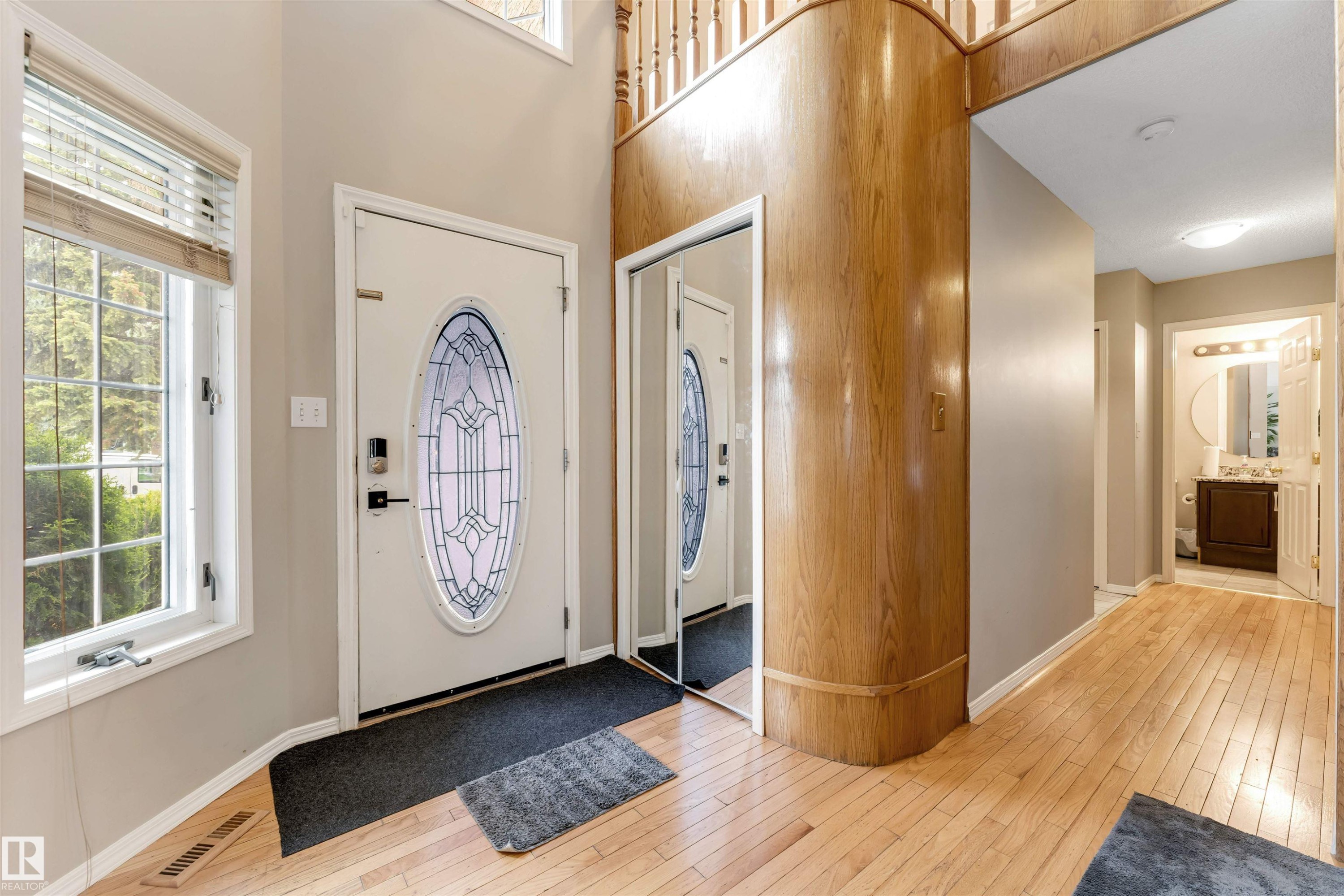 Entryway featuring a decorative oval-insert front door, hardwood flooring, and a large window with horizontal blinds - 4465 32A Street Nw, Edmonton, AB - Indoor Photo Showing Other Room