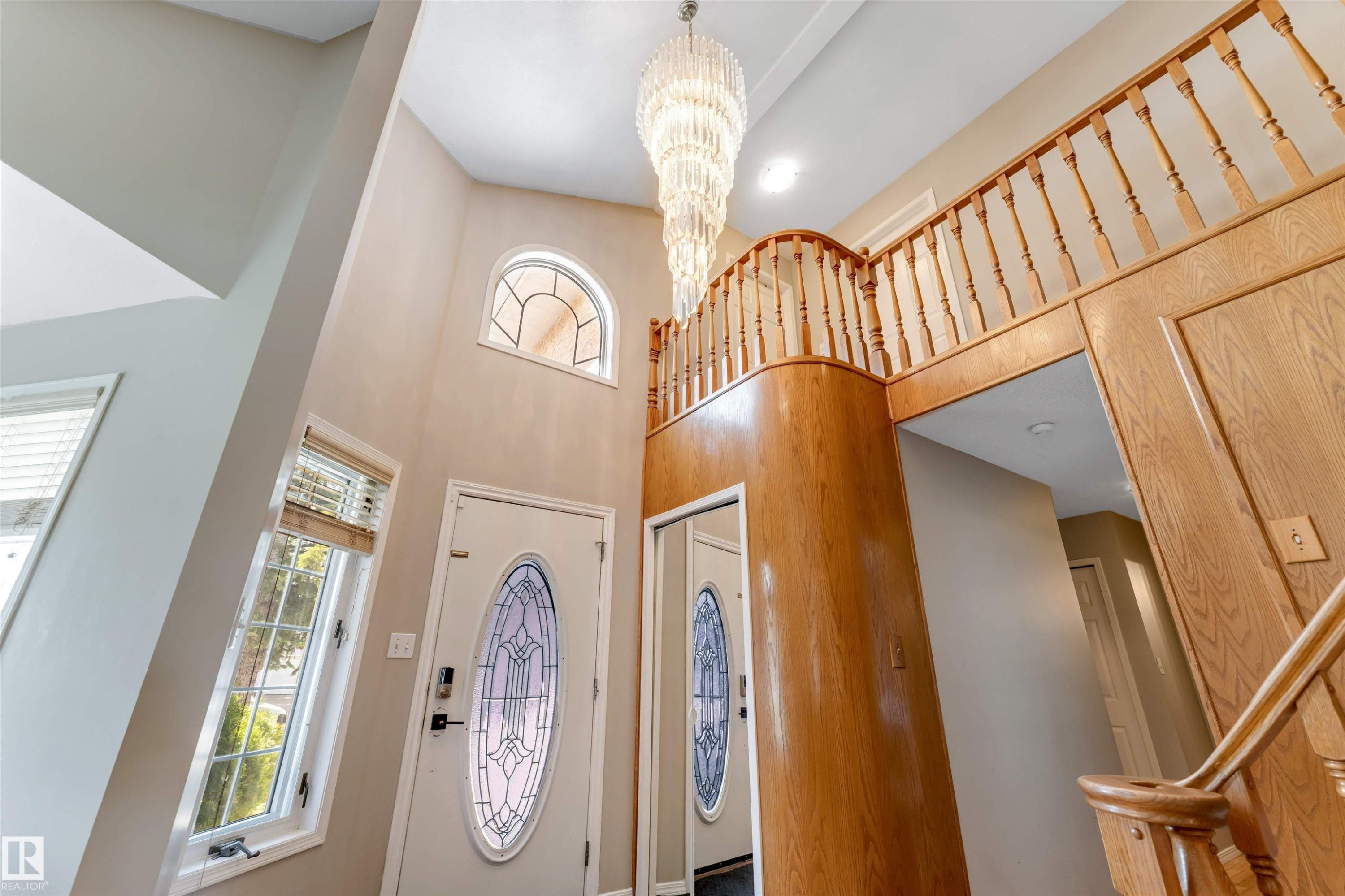 Two-story foyer featuring an ornate chandelier, a decorative arched window, a paneled wooden staircase, and a front entry door with leaded glass - 4465 32A Street Nw, Edmonton, AB - Indoor Photo Showing Other Room