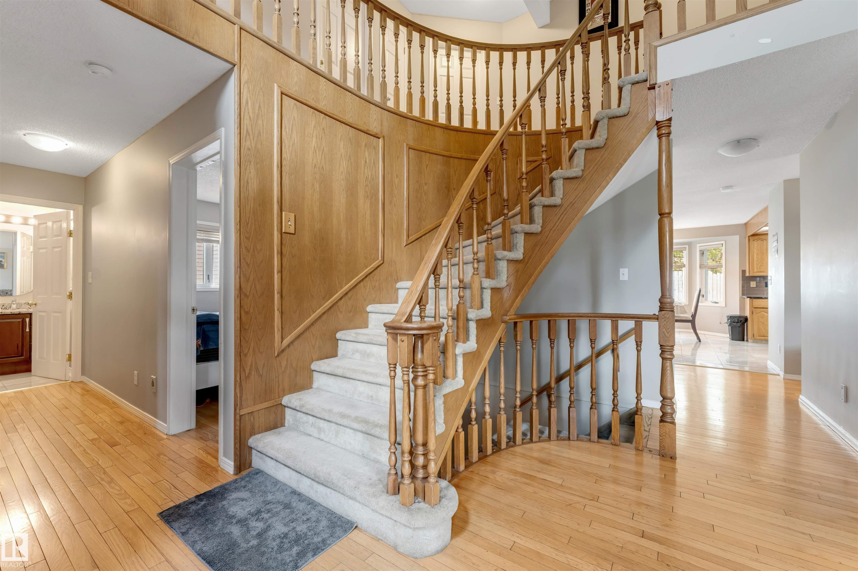 Elegant curved staircase with wood balusters and carpeted treads - 4465 32A Street Nw, Edmonton, AB - Indoor Photo Showing Other Room