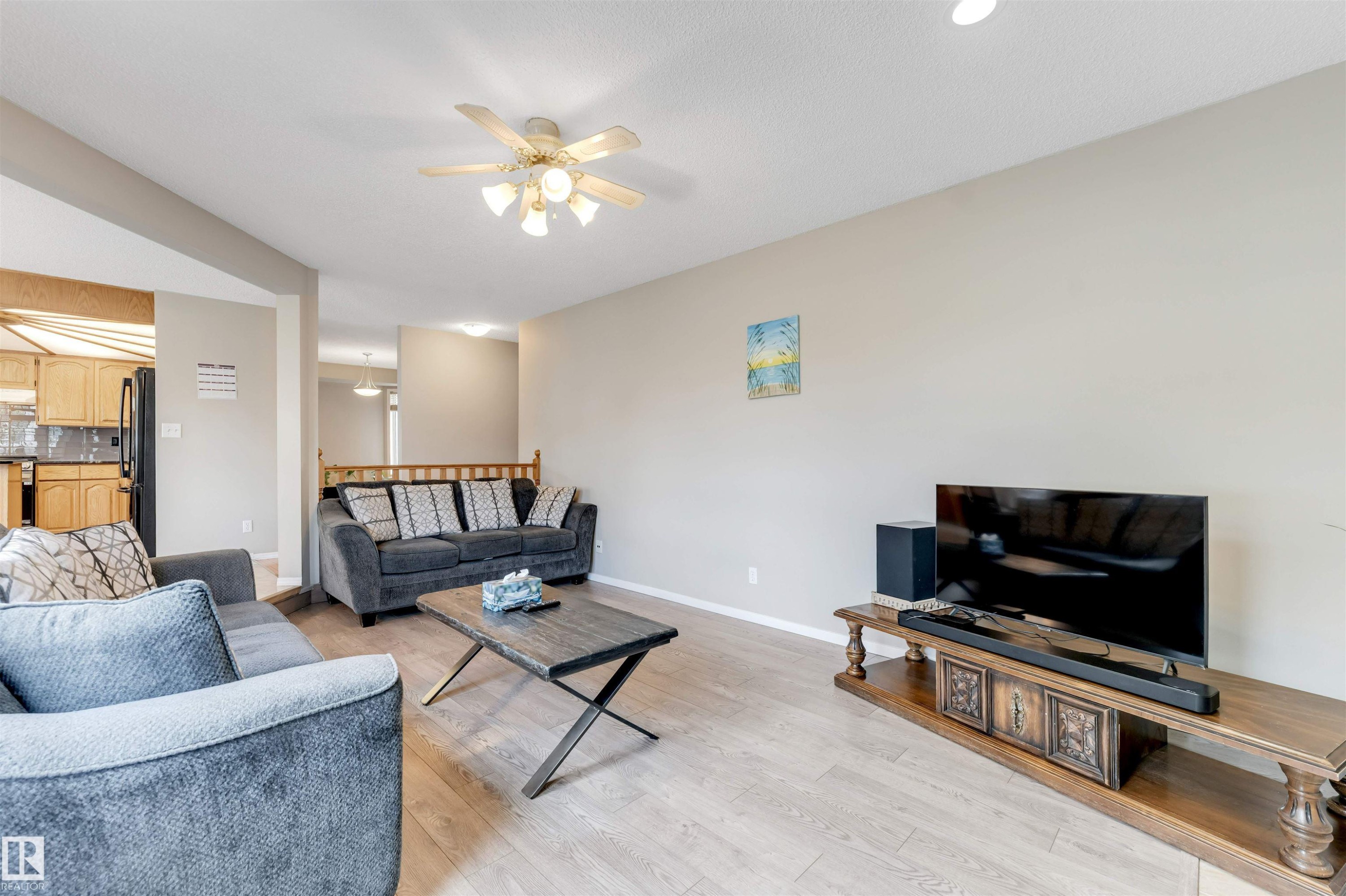 Spacious living area featuring light wood-finish flooring, neutral wall tones, and a ceiling fan with integrated lighting - 4465 32A Street Nw, Edmonton, AB - Indoor Photo Showing Living Room