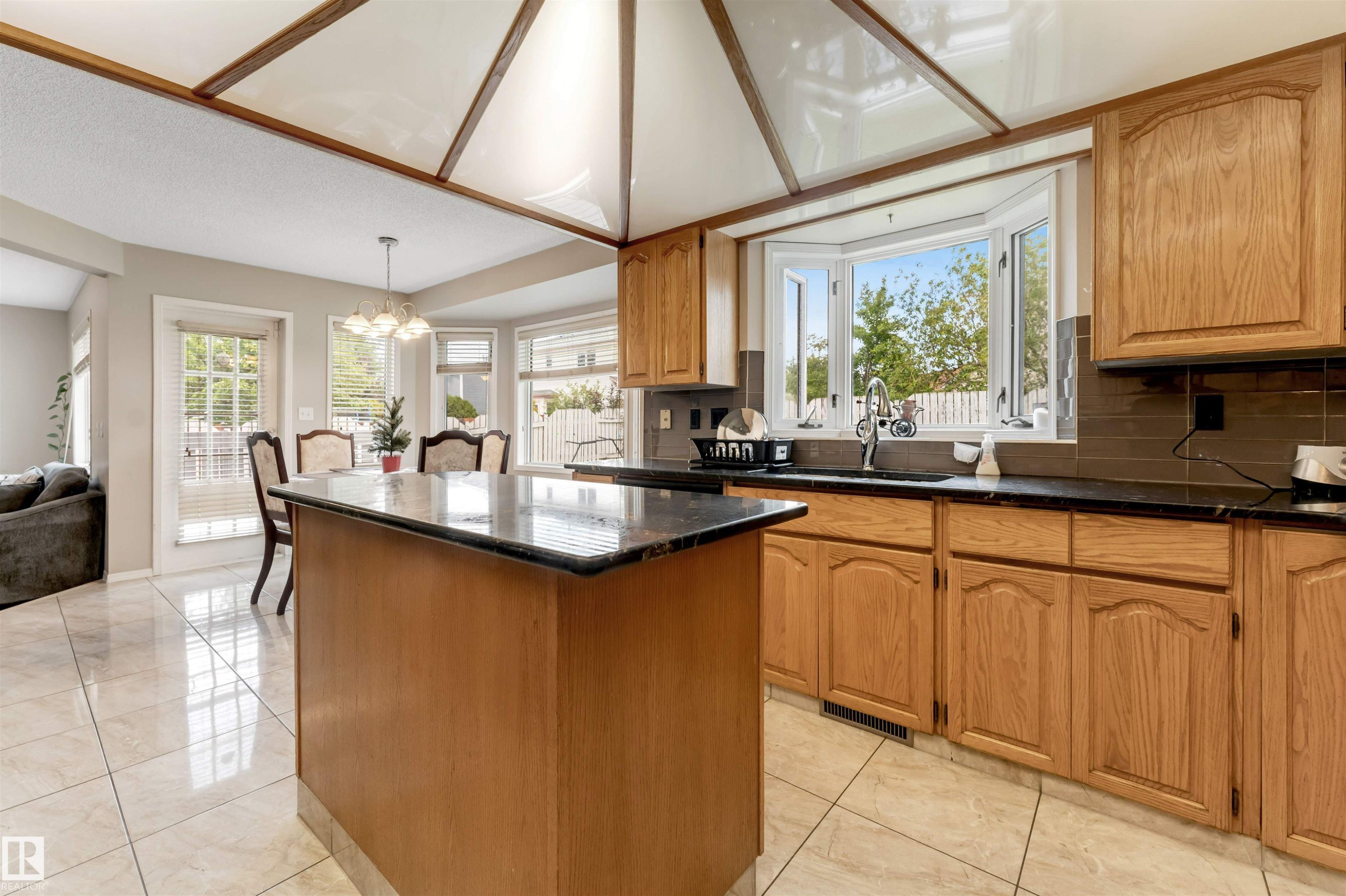 Kitchen featuring a central island with a dark countertop, wood-finish cabinetry, tile flooring, and a bay window - 4465 32A Street Nw, Edmonton, AB - Indoor Photo Showing Kitchen