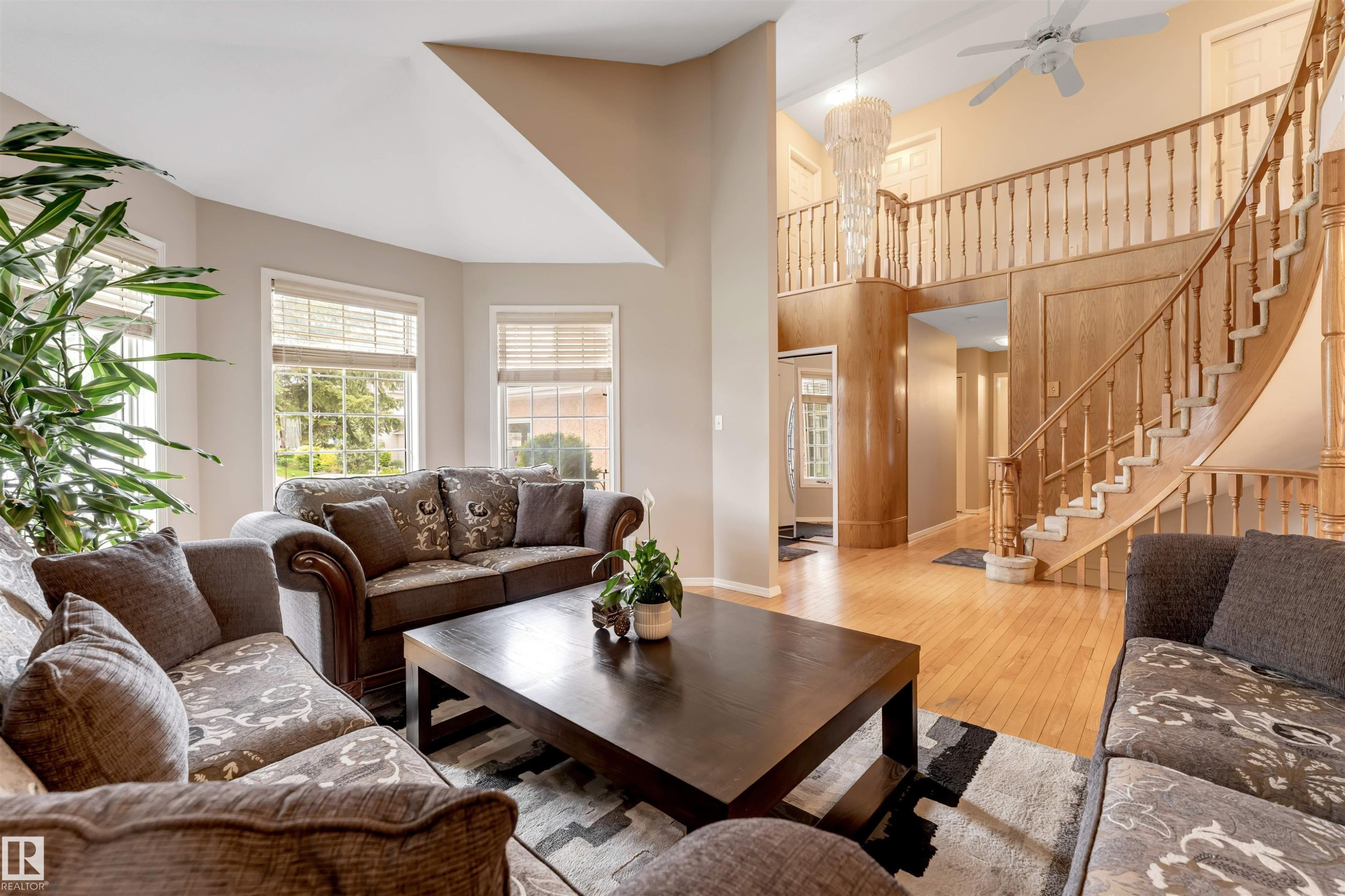 Two-story foyer featuring a curved staircase with wood balusters, a large chandelier, and a second-story balcony - 4465 32A Street Nw, Edmonton, AB - Indoor Photo Showing Living Room