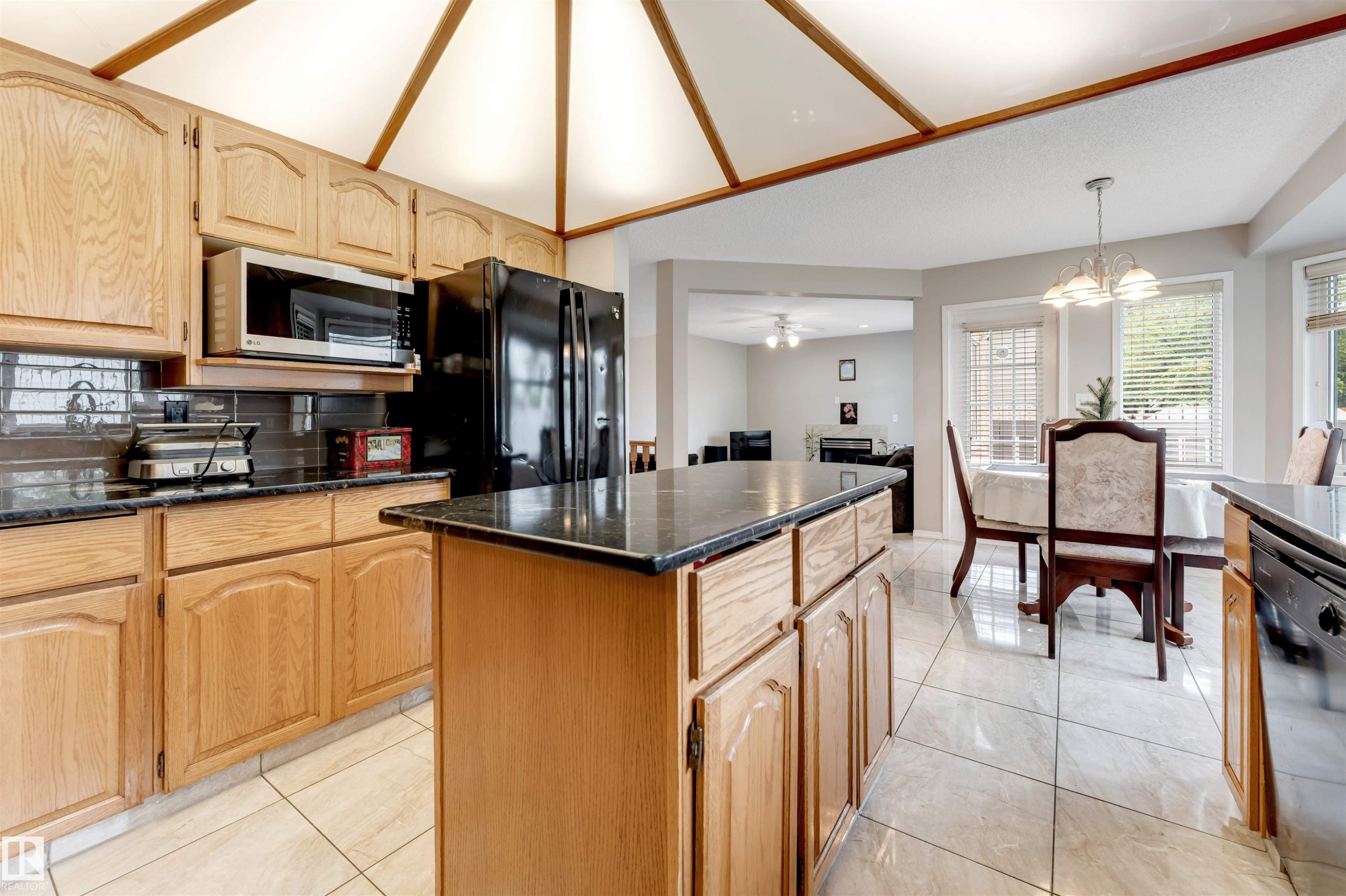 Kitchen featuring wood cabinetry, dark countertops, tile flooring, and a vaulted ceiling with wood accents - 4465 32A Street Nw, Edmonton, AB - Indoor Photo Showing Kitchen