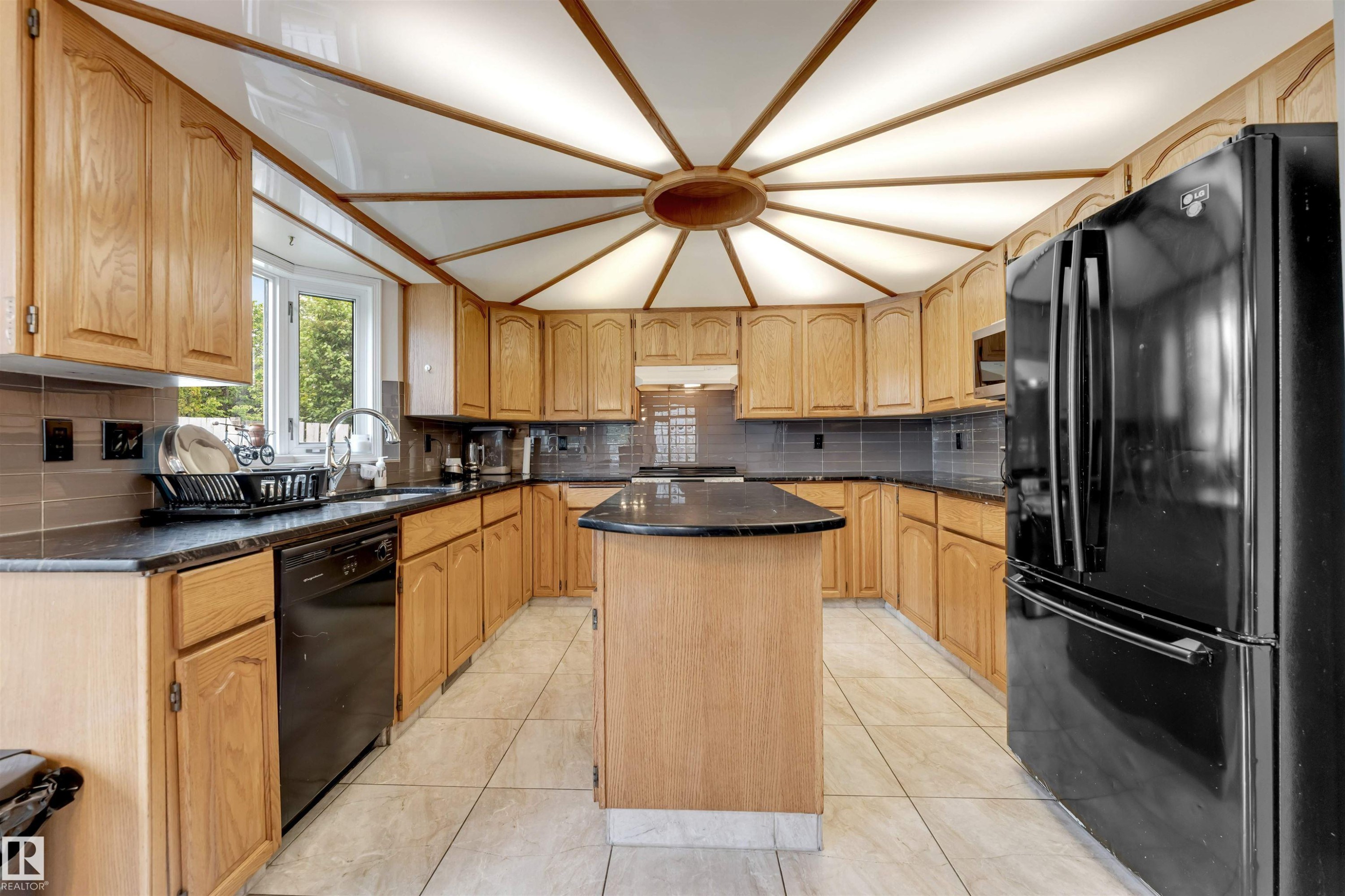 Kitchen featuring a central island, light wood cabinetry, dark countertops, and a radial ceiling design - 4465 32A Street Nw, Edmonton, AB - Indoor Photo Showing Kitchen