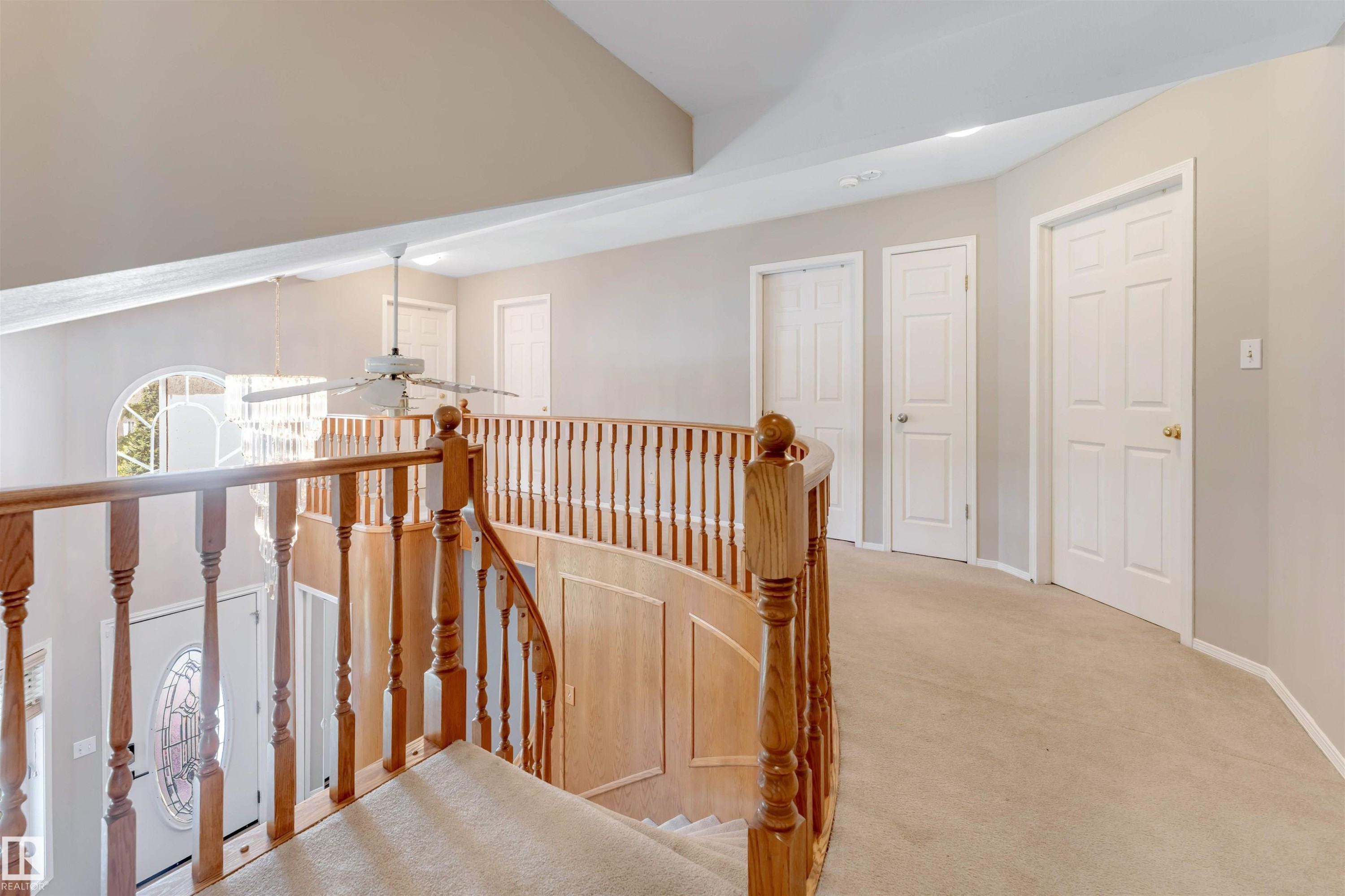 Upper-level landing featuring a curved wood banister, carpeted flooring, and multiple paneled doors - 4465 32A Street Nw, Edmonton, AB - Indoor Photo Showing Other Room