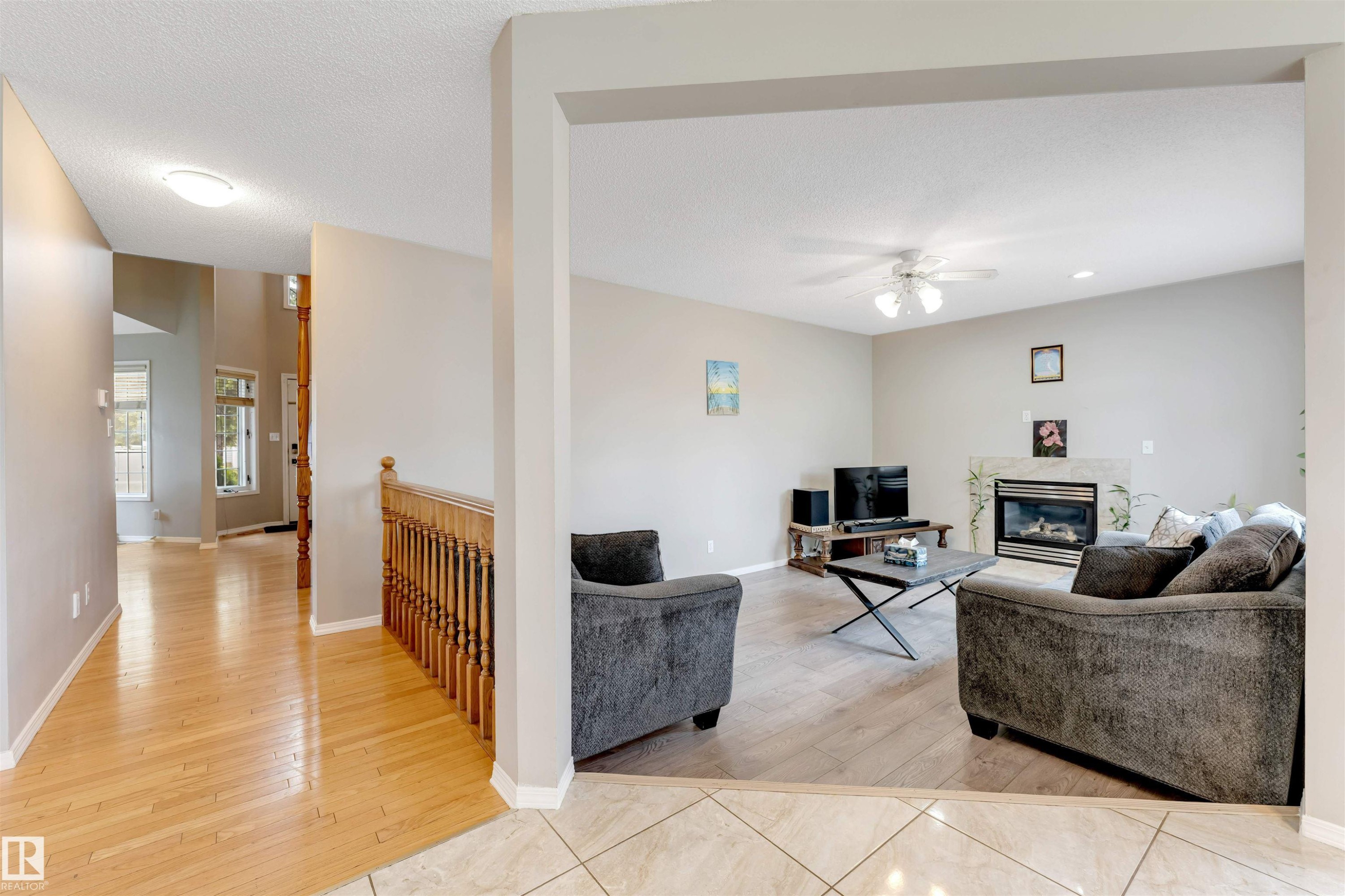 Living area featuring a gas fireplace with a stone surround, a ceiling fan, and wood-finish flooring - 4465 32A Street Nw, Edmonton, AB - Indoor With Fireplace