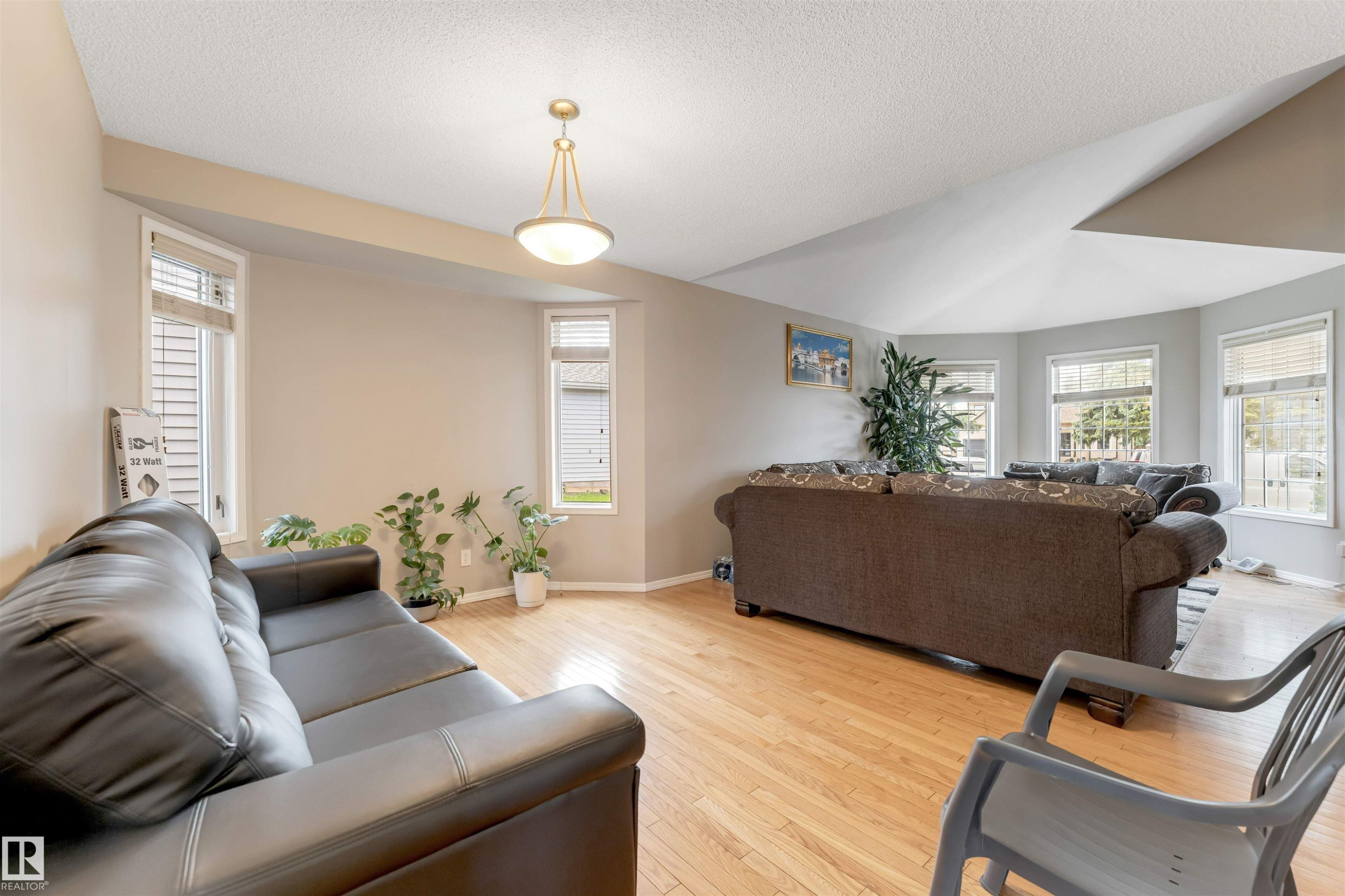 Spacious living area featuring light wood-finish flooring, multiple large windows with white trim, and a contemporary ceiling light fixture - 4465 32A Street Nw, Edmonton, AB - Indoor Photo Showing Living Room