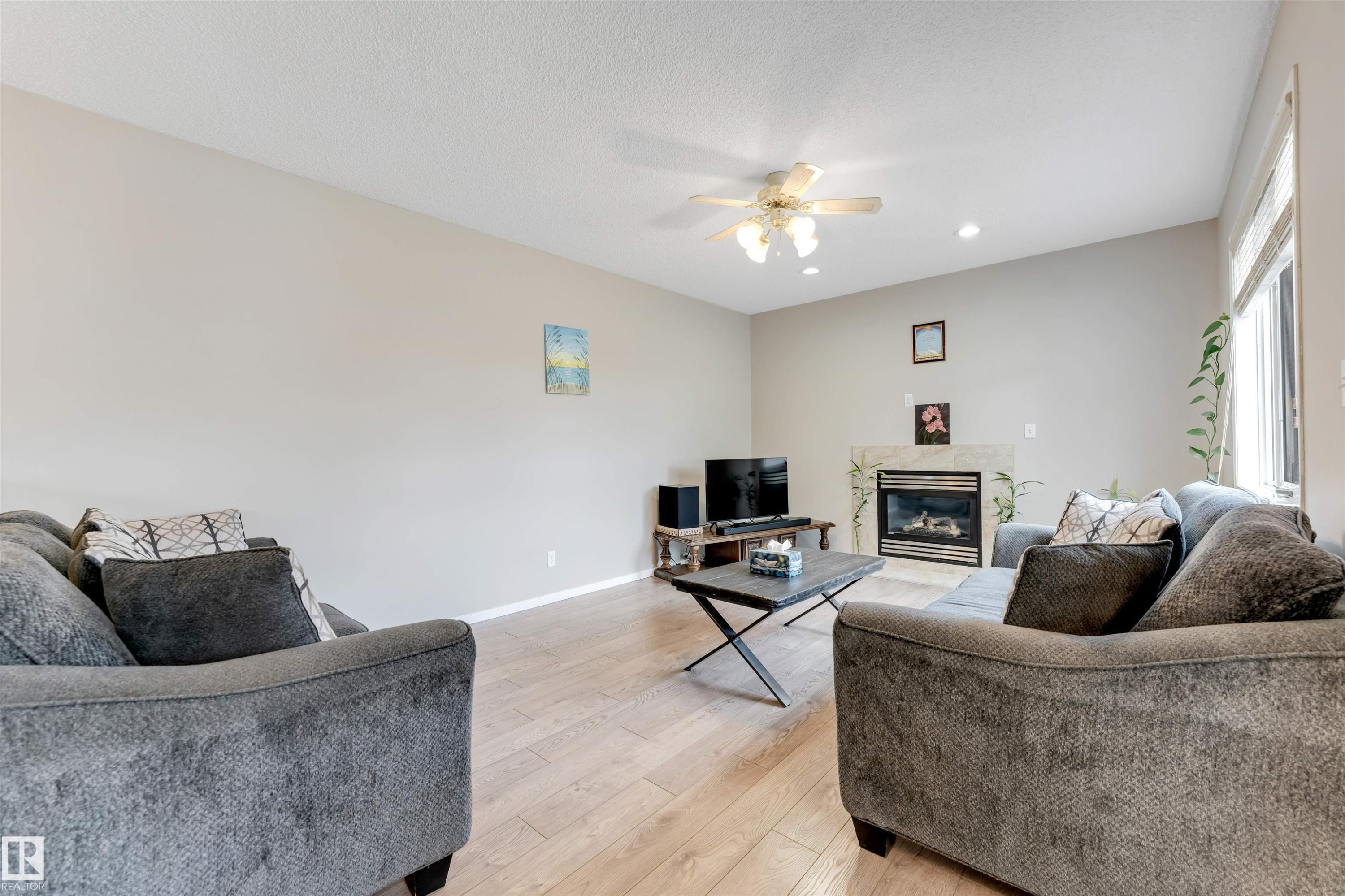 Spacious living area featuring light wood-finish flooring, a contemporary fireplace with a stone surround, and recessed lighting - 4465 32A Street Nw, Edmonton, AB - Indoor Photo Showing Living Room With Fireplace
