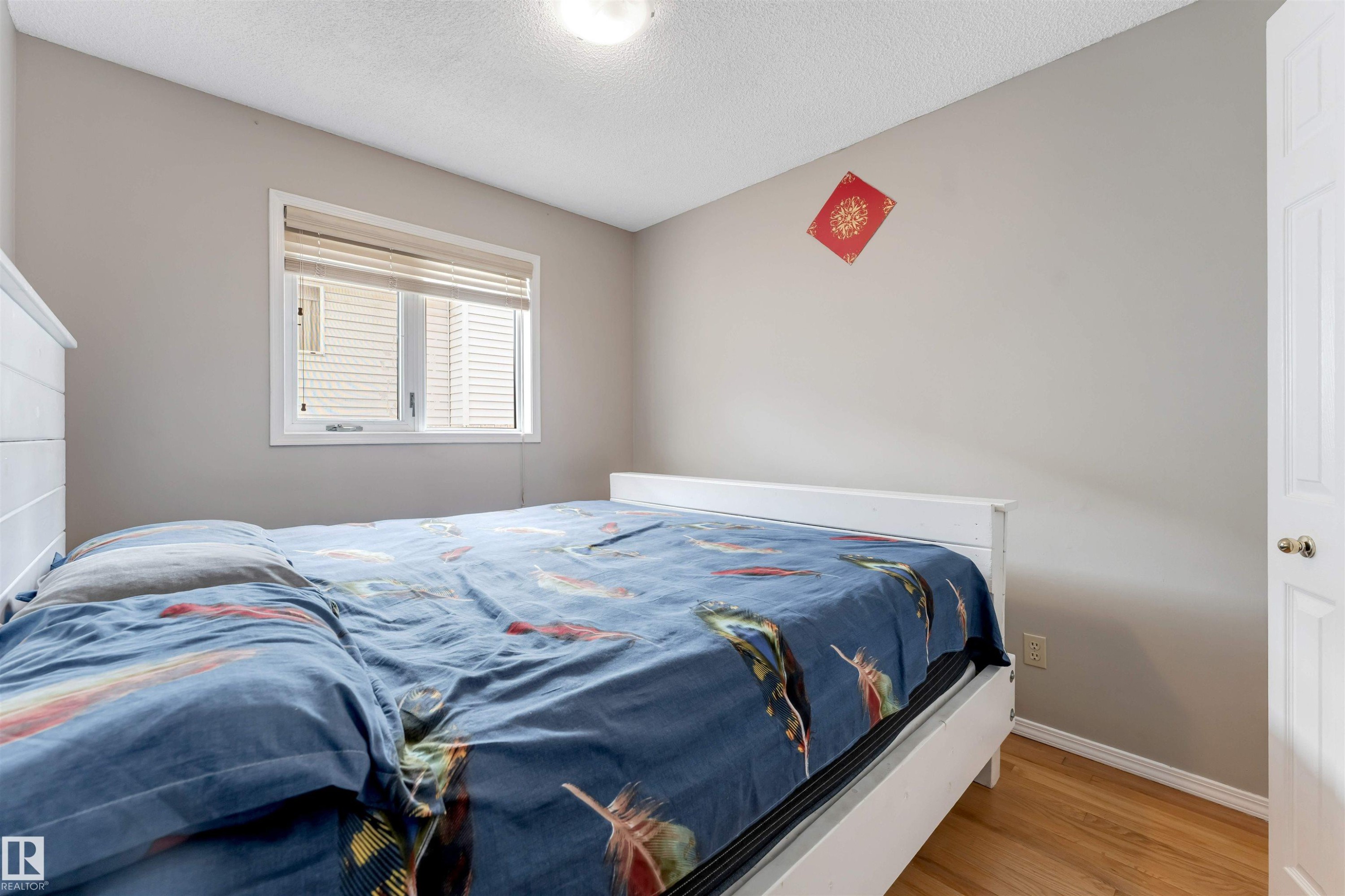 Bedroom featuring light gray wall paint, wood-finish flooring, a white window frame with blinds, and a white paneled door - 4465 32A Street Nw, Edmonton, AB - Indoor Photo Showing Bedroom