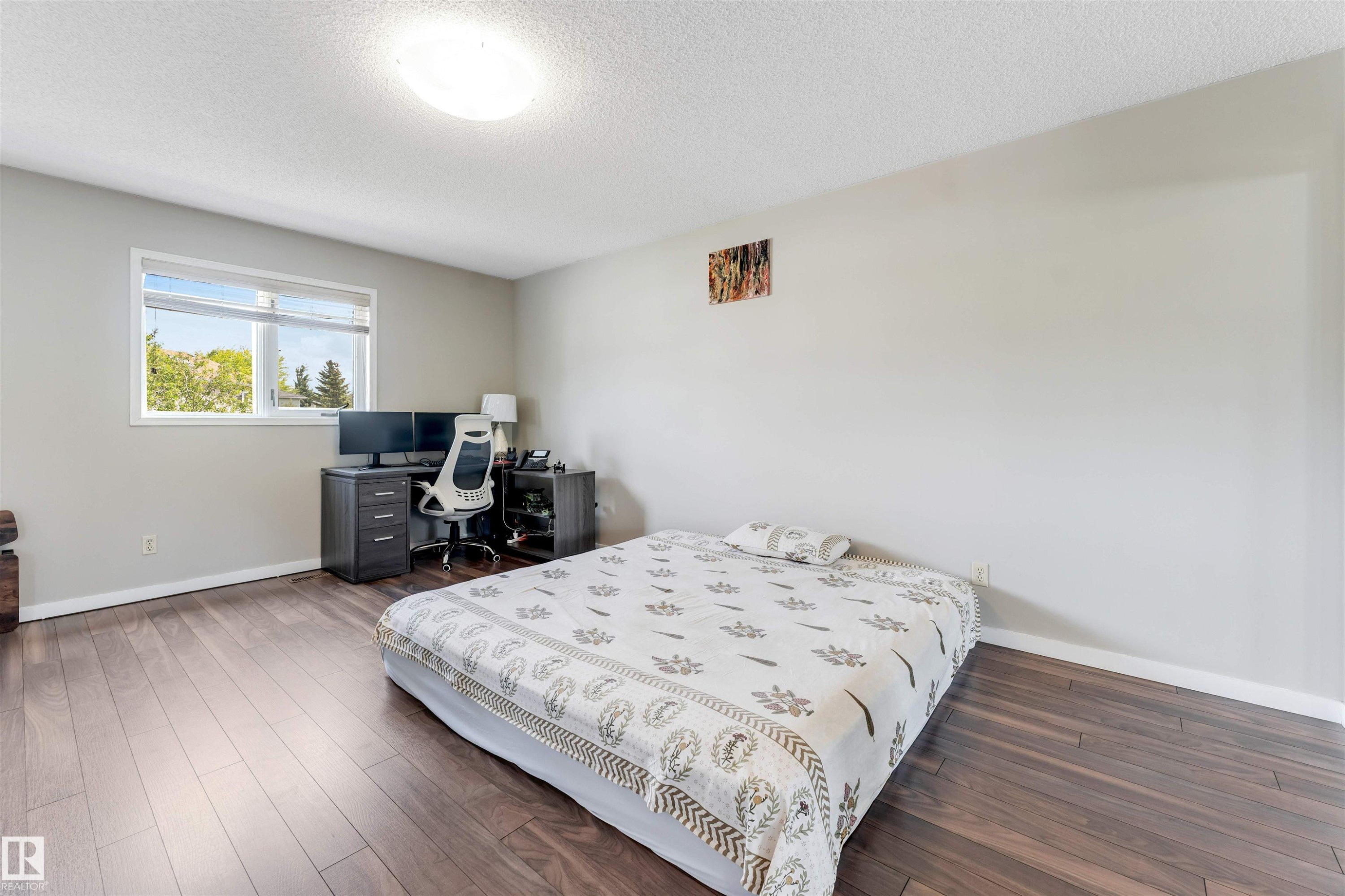 Spacious room featuring wood-finish flooring, a large window, light-toned walls, and a ceiling-mounted light fixture - 4465 32A Street Nw, Edmonton, AB - Indoor Photo Showing Bedroom