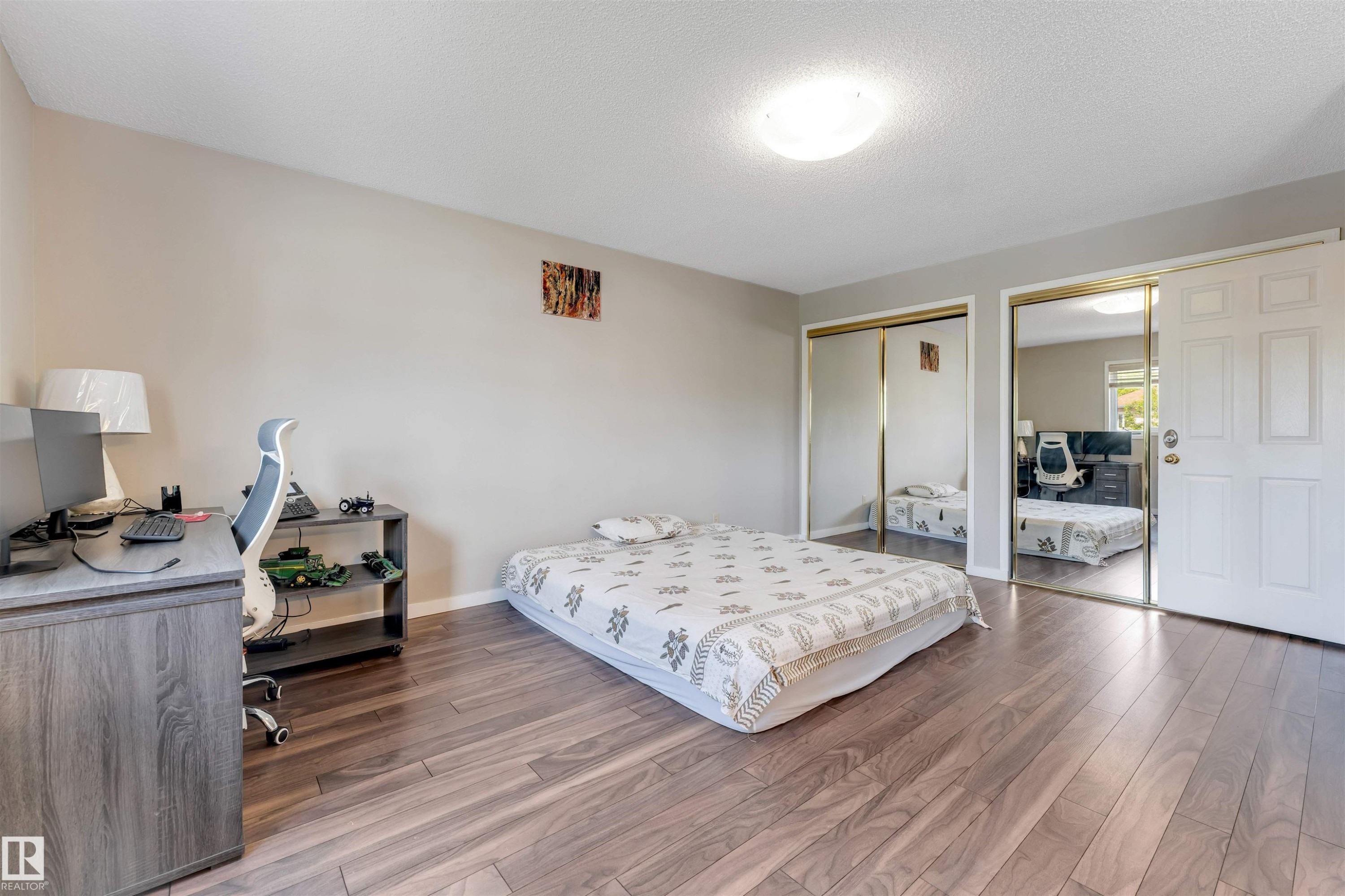 Spacious room featuring wood-finish flooring, two mirrored sliding closet doors, and light neutral wall paint - 4465 32A Street Nw, Edmonton, AB - Indoor Photo Showing Bedroom