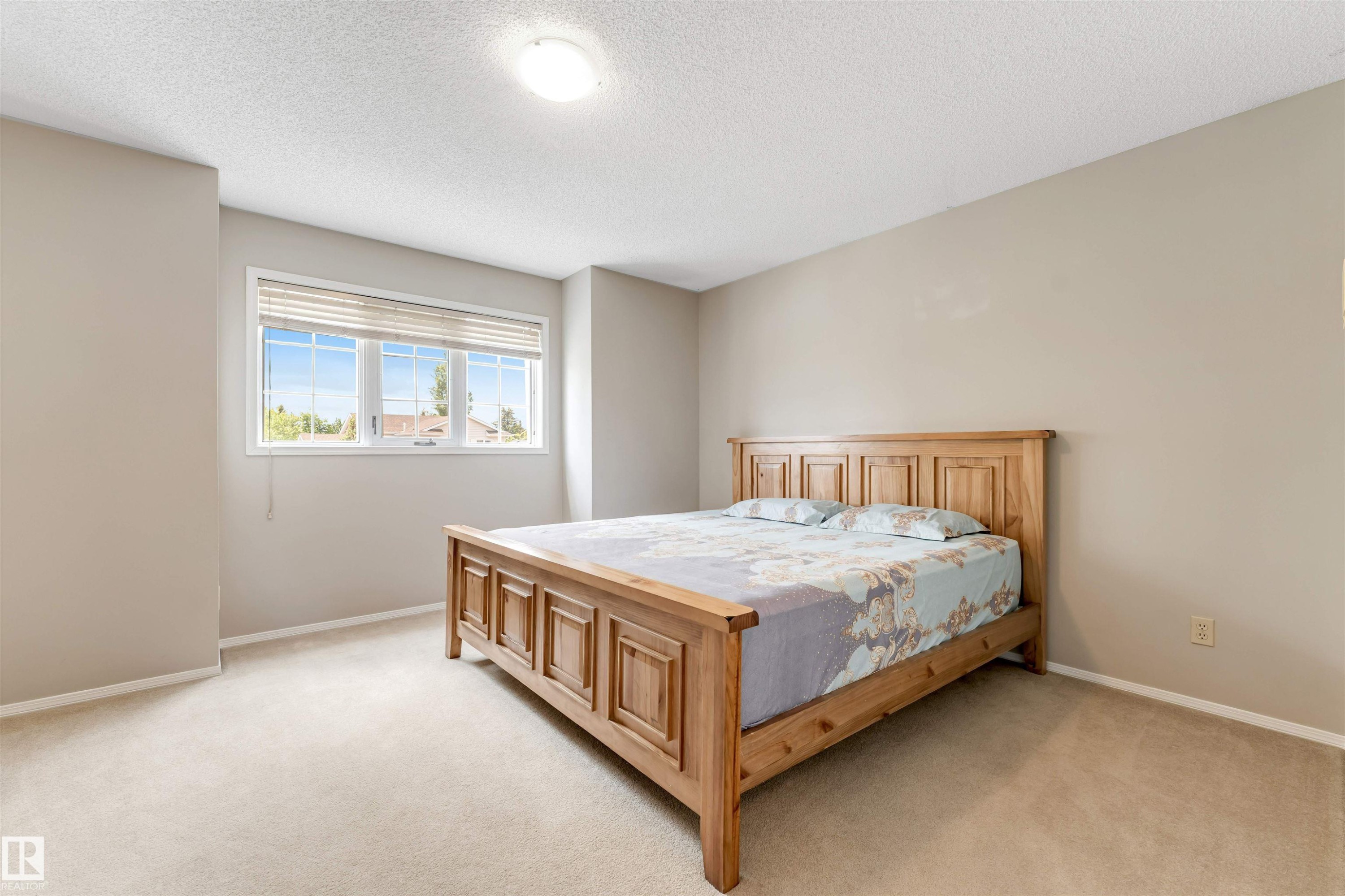 Carpeted bedroom featuring a large window with horizontal blinds, neutral wall tones, and a ceiling-mounted light fixture - 4465 32A Street Nw, Edmonton, AB - Indoor Photo Showing Bedroom