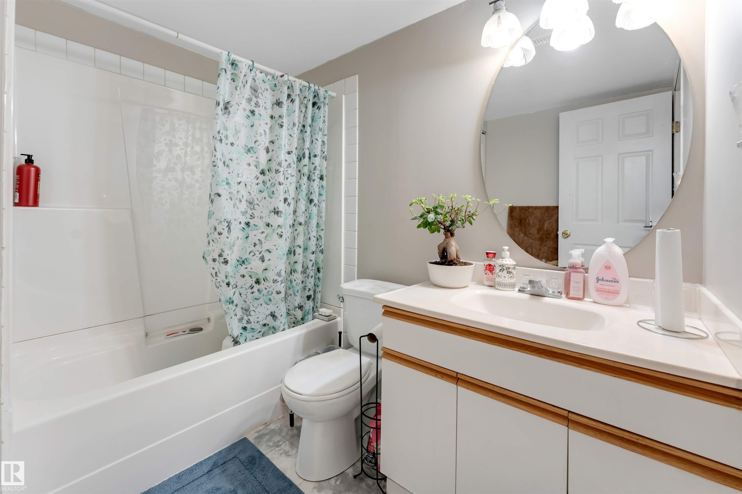 Bathroom featuring a vanity with an integrated sink, a large circular mirror, and a tub-shower combination with a tiled surround - 4465 32A Street Nw, Edmonton, AB - Indoor Photo Showing Bathroom