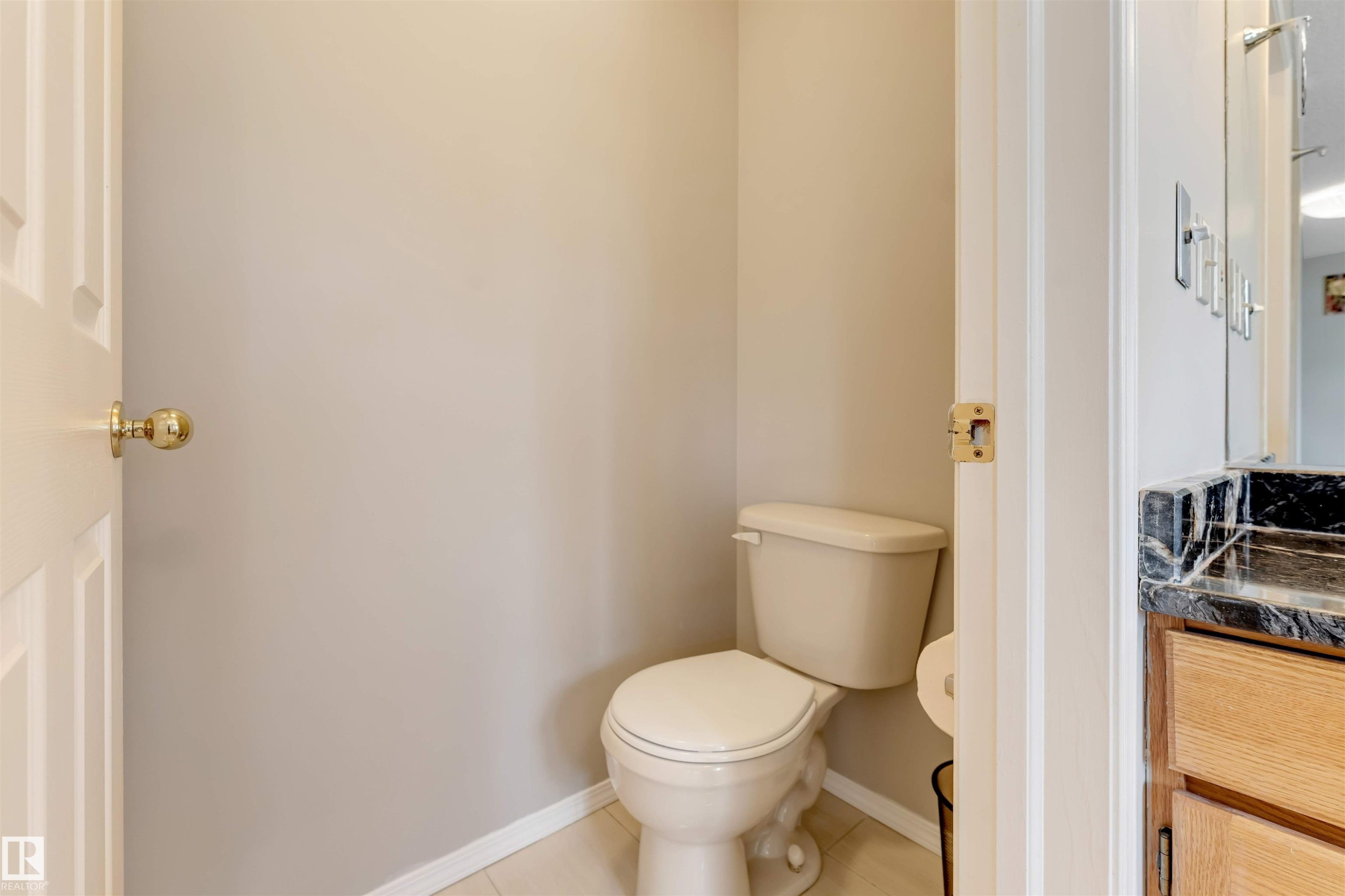 Powder room featuring a ceramic toilet, light neutral wall color, and tile flooring - 4465 32A Street Nw, Edmonton, AB - Indoor Photo Showing Bathroom