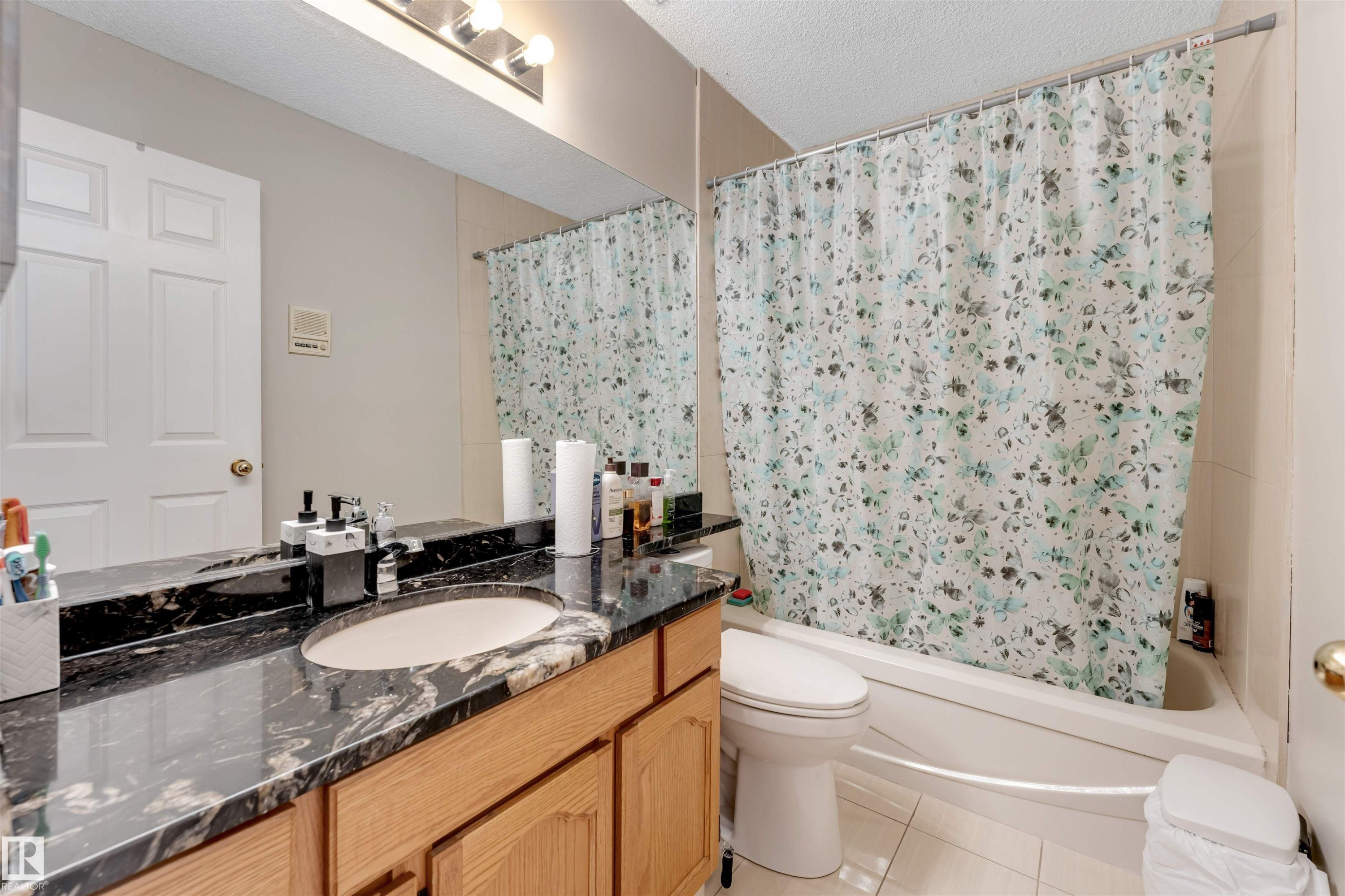 Bathroom vanity featuring a black stone countertop with an undermount sink, wood-finish cabinetry, and an overhead light fixture - 4465 32A Street Nw, Edmonton, AB - Indoor Photo Showing Bathroom