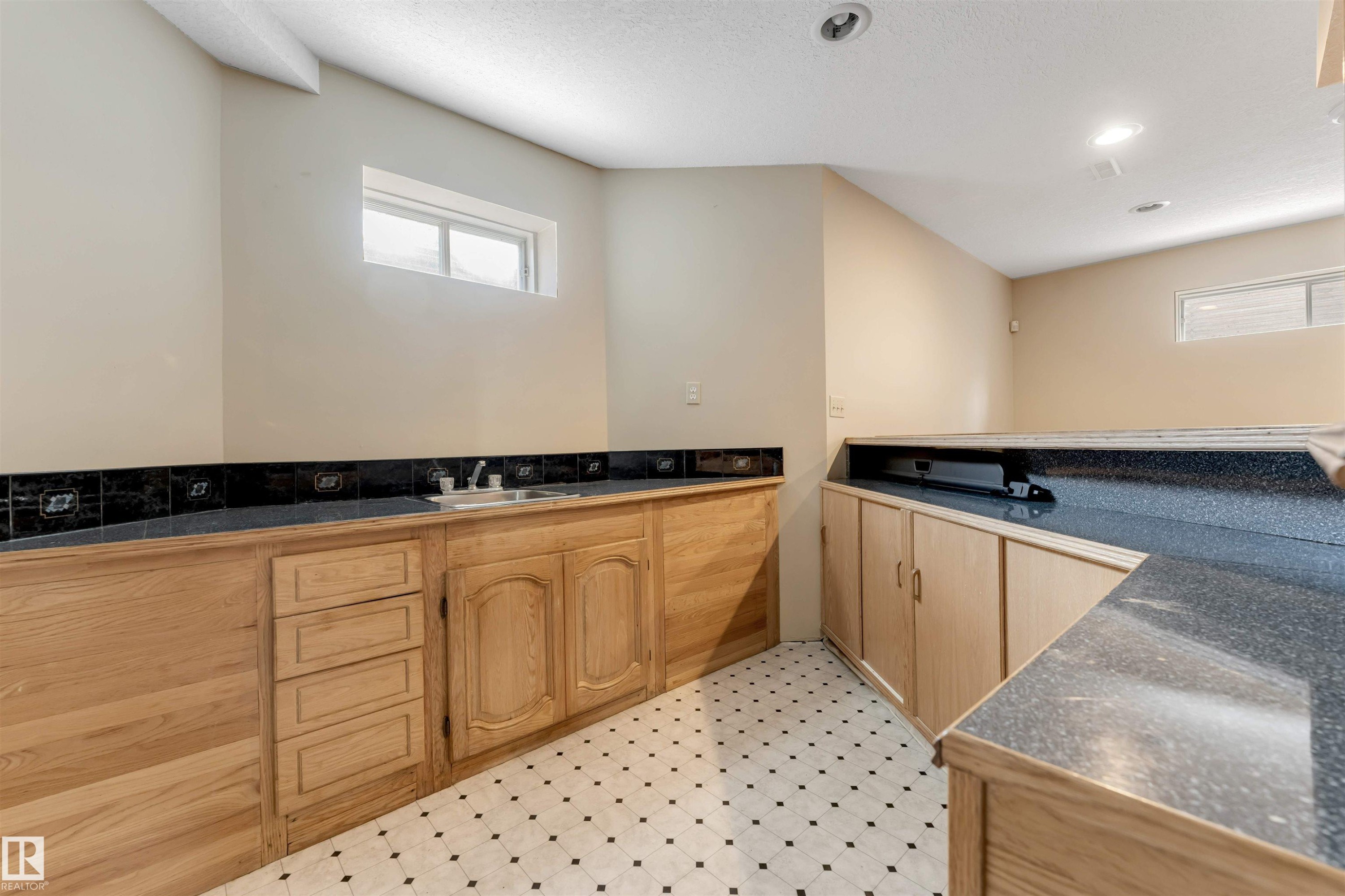 Utility space featuring extensive counter surfaces, light wood cabinetry, and a black and white geometric tile floor - 4465 32A Street Nw, Edmonton, AB - Indoor Photo Showing Other Room