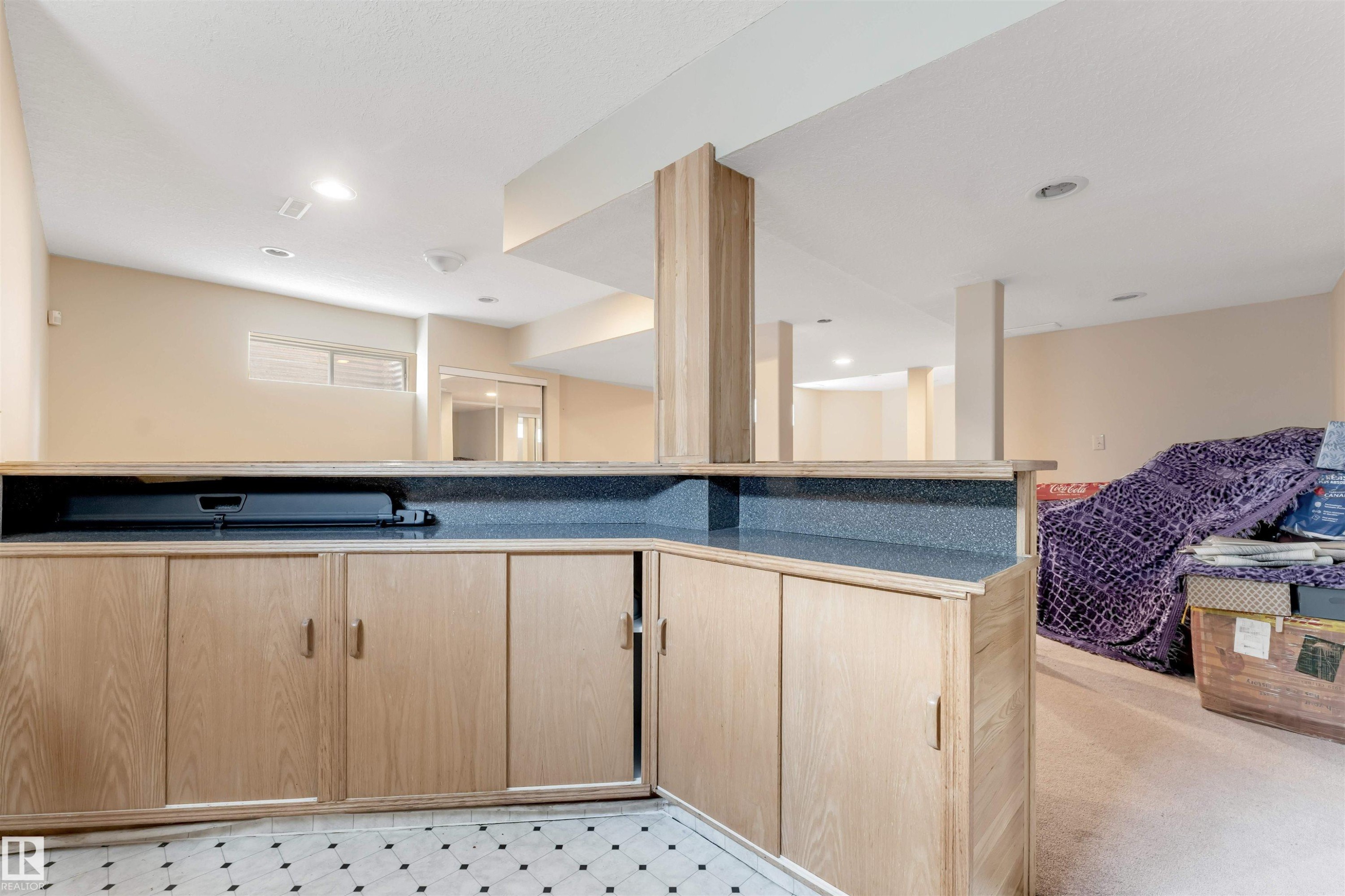 Recessed lighting illuminates this room featuring light wood-finish cabinetry with brass hardware, a dark speckled countertop, and a black and white patterned tile floor - 4465 32A Street Nw, Edmonton, AB - Indoor