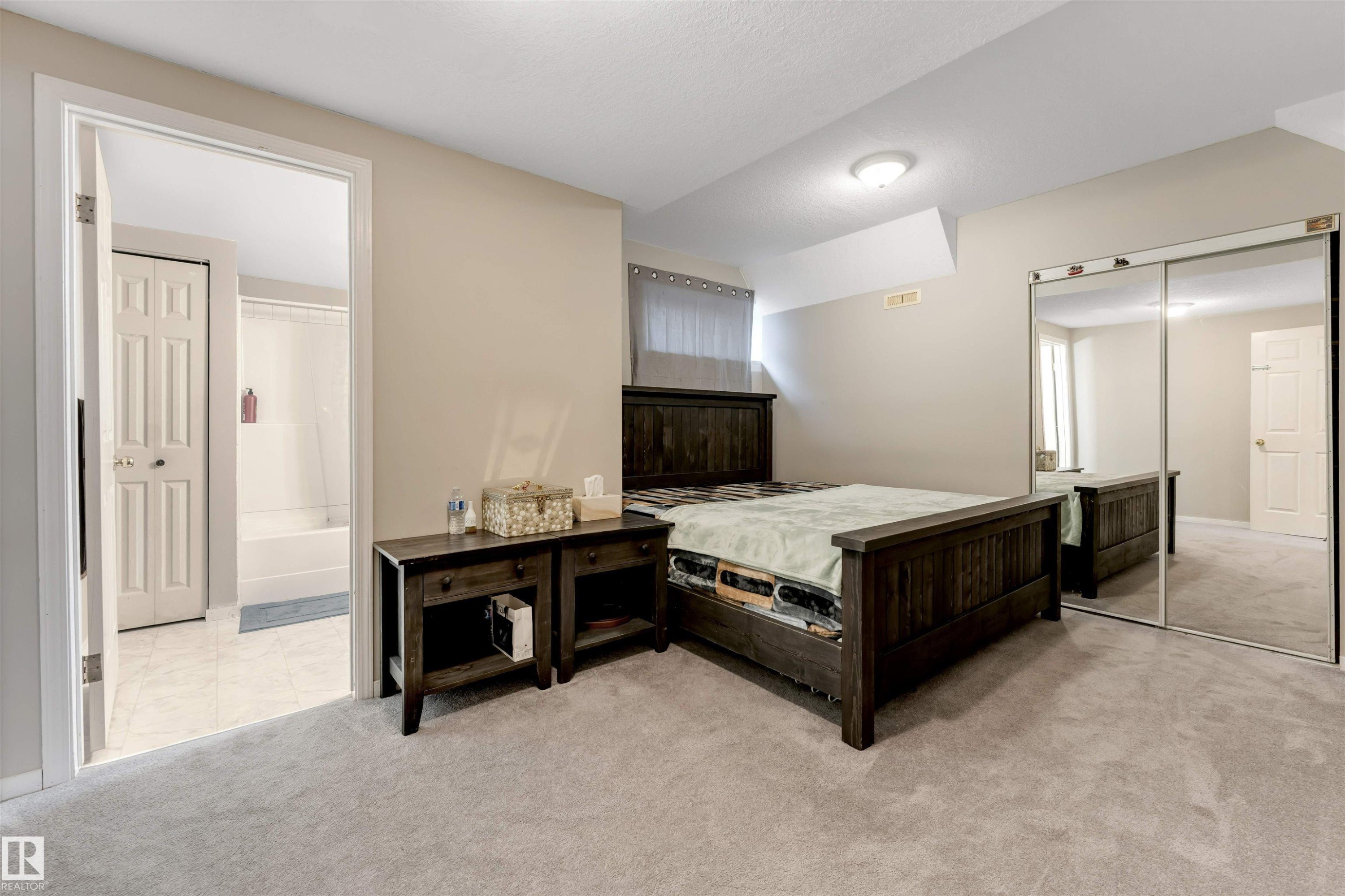 Carpeted bedroom featuring a full-length mirrored closet and direct access to a bathroom with tiled flooring and a white shower/tub combination - 4465 32A Street Nw, Edmonton, AB - Indoor Photo Showing Bedroom