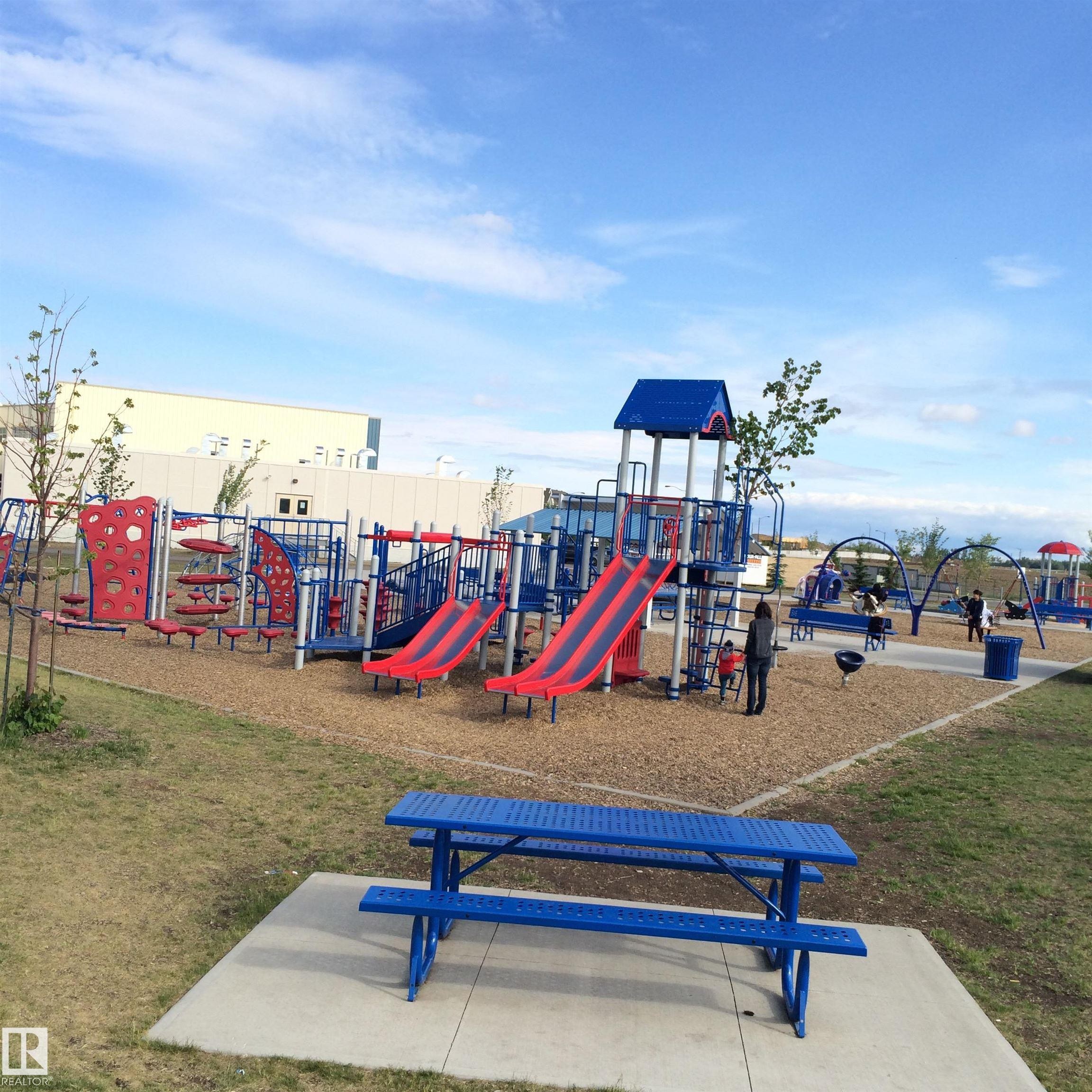 Expansive recreational area featuring multiple play structures, a picnic table on a concrete pad, and a wood chip surface - 1839 80 Street Sw, Edmonton, AB