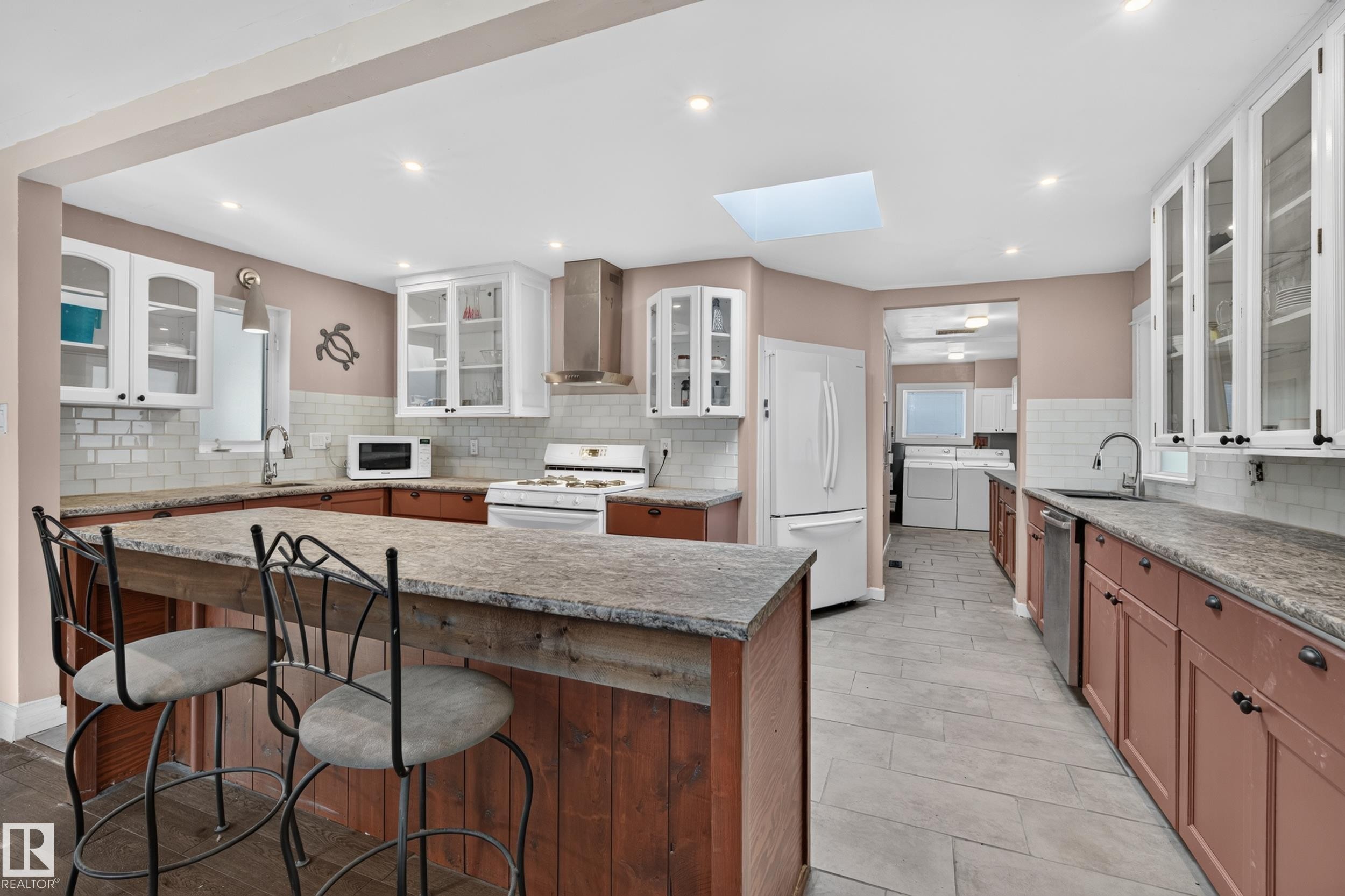 Kitchen featuring a skylight, recessed lighting, white subway tile backsplash, white upper cabinetry, and a peninsula with seating - 11603 72 Avenue Nw, Edmonton, AB