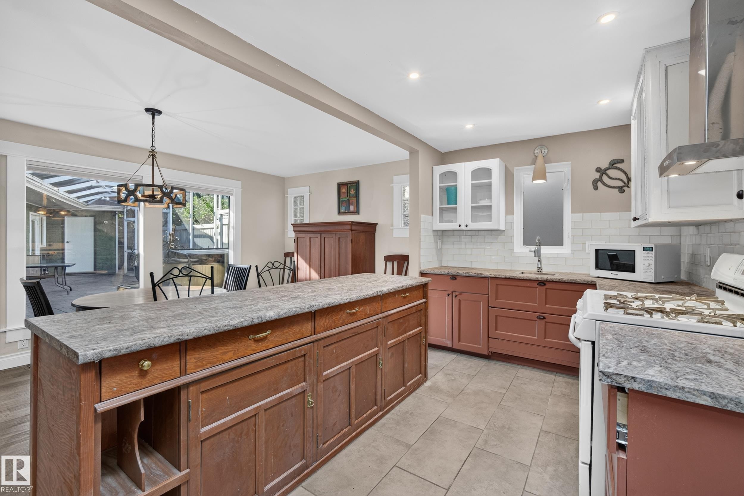 Kitchen featuring a large island with a stone-finish countertop, tile flooring, white subway tile backsplash, and stainless steel range hood - 11603 72 Avenue Nw, Edmonton, AB