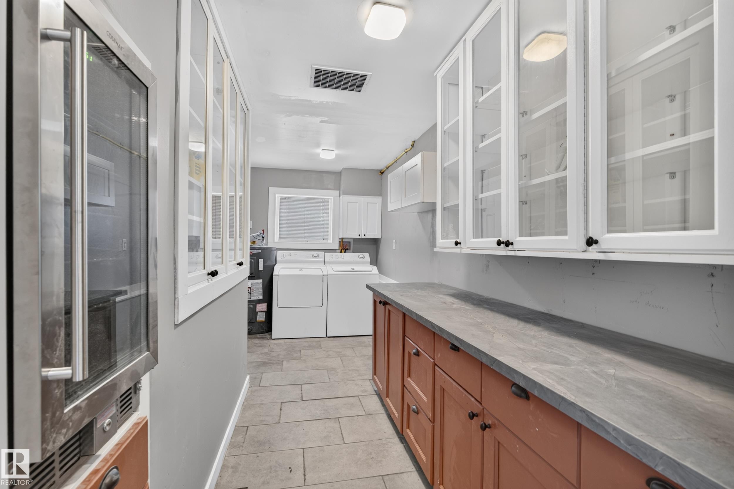 Integrated beverage cooler, white upper cabinetry with glass inserts, wood-finish base cabinetry, gray countertop surface, and tile flooring - 11603 72 Avenue Nw, Edmonton, AB