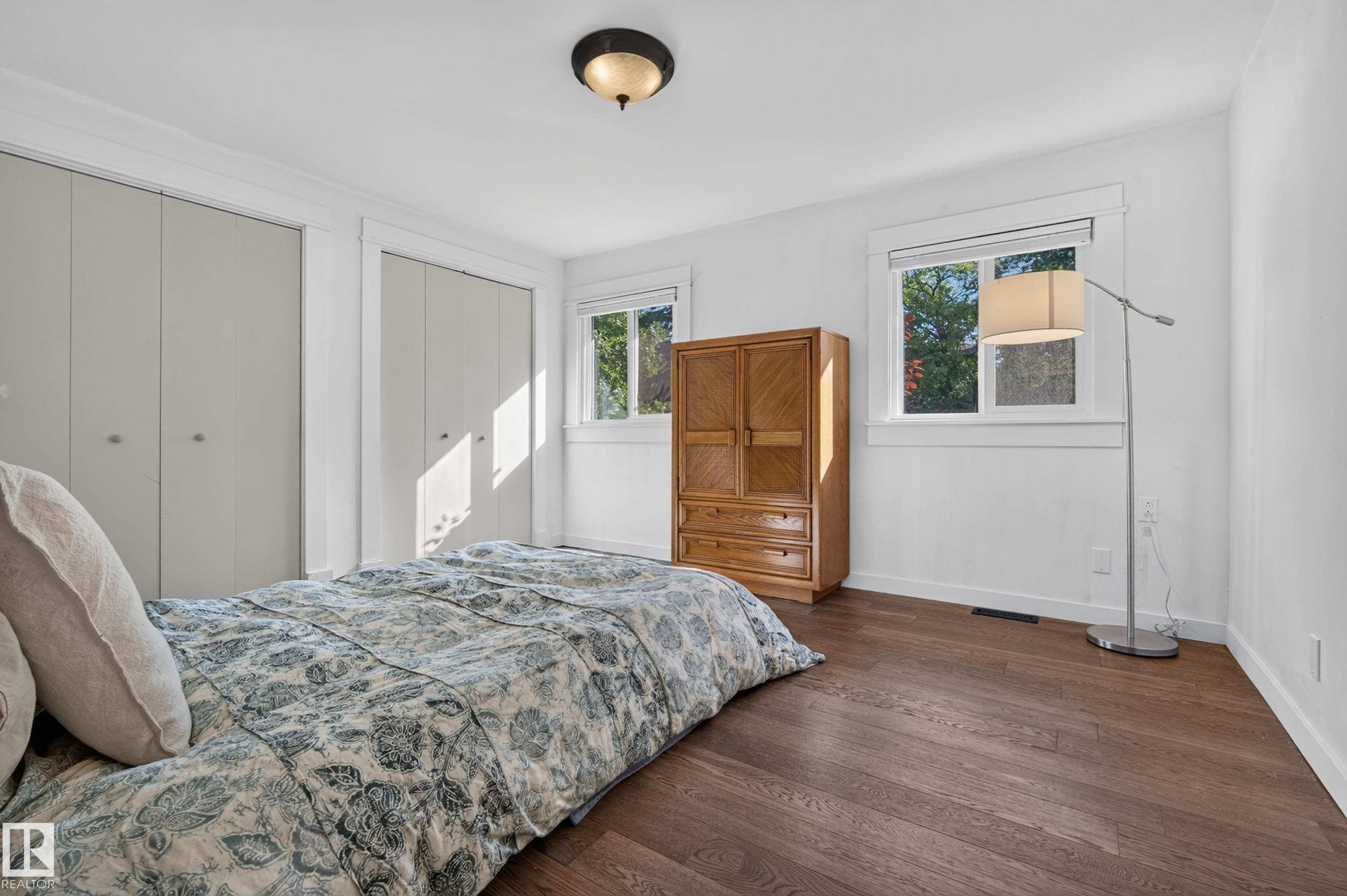 Hardwood flooring, white painted walls, two windows, two bi-fold closets, and a semi-flush mount ceiling light fixture - 11603 72 Avenue Nw, Edmonton, AB