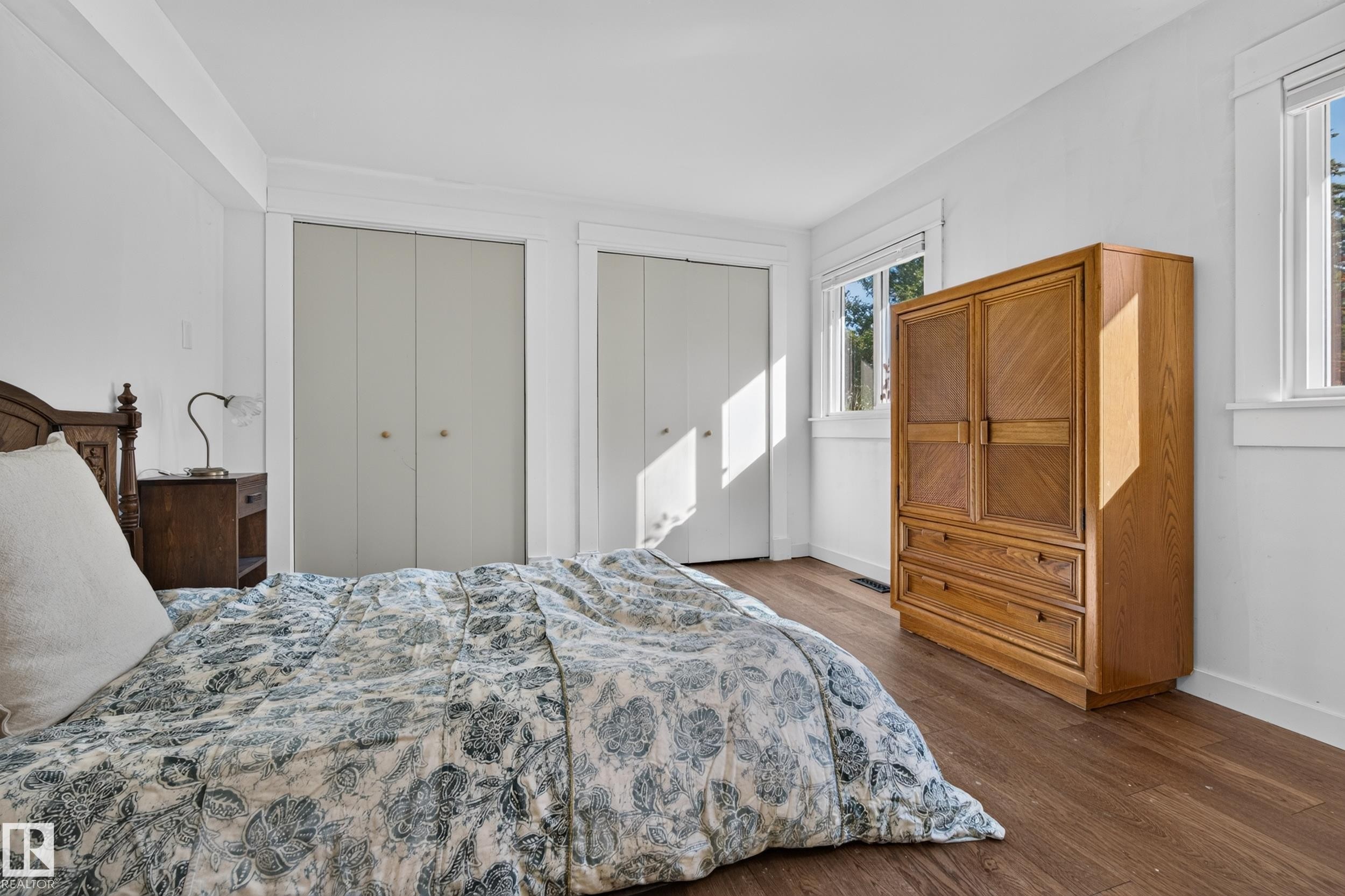 Wood-finish flooring with white trim, two white bi-fold closets, and multiple windows - 11603 72 Avenue Nw, Edmonton, AB