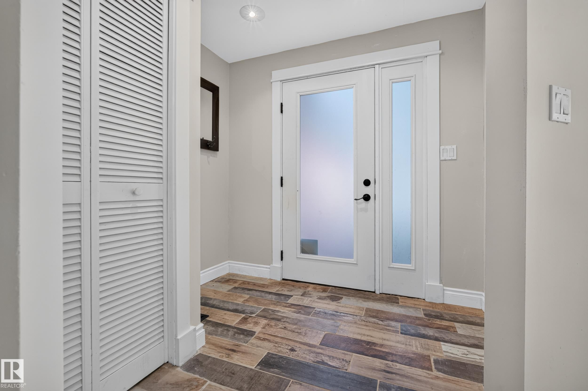Entryway featuring wood-finish flooring, a white front door with frosted glass, a coordinating frosted glass sidelight, and white louvered bifold closet doors - 11603 72 Avenue Nw, Edmonton, AB